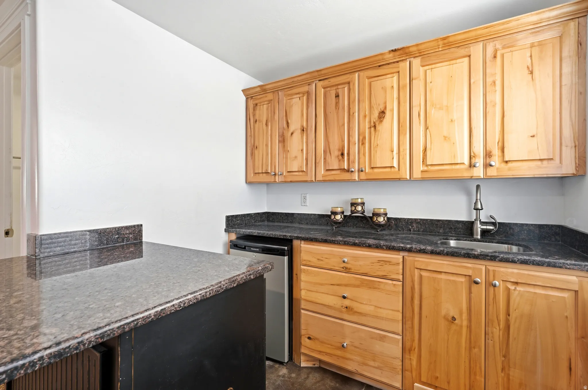 Natural wood cabinetry with brushed nickel hardware, dark speckled countertops, and an undermount stainless steel sink