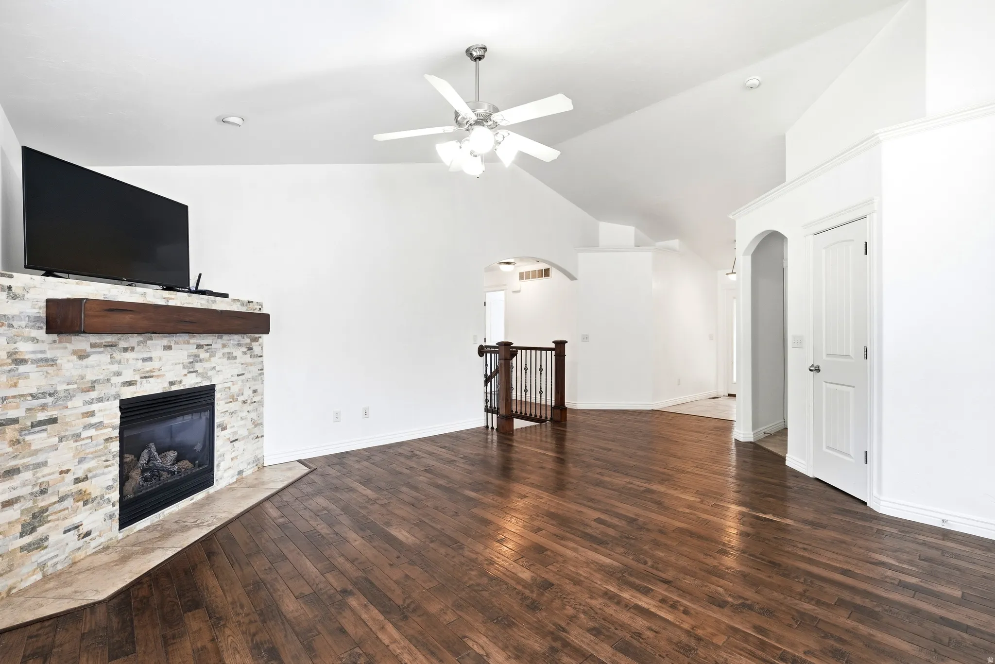 Spacious interior featuring a stacked stone fireplace with a wood mantel, rich wood-finish flooring, and vaulted ceilings with a ceiling fan