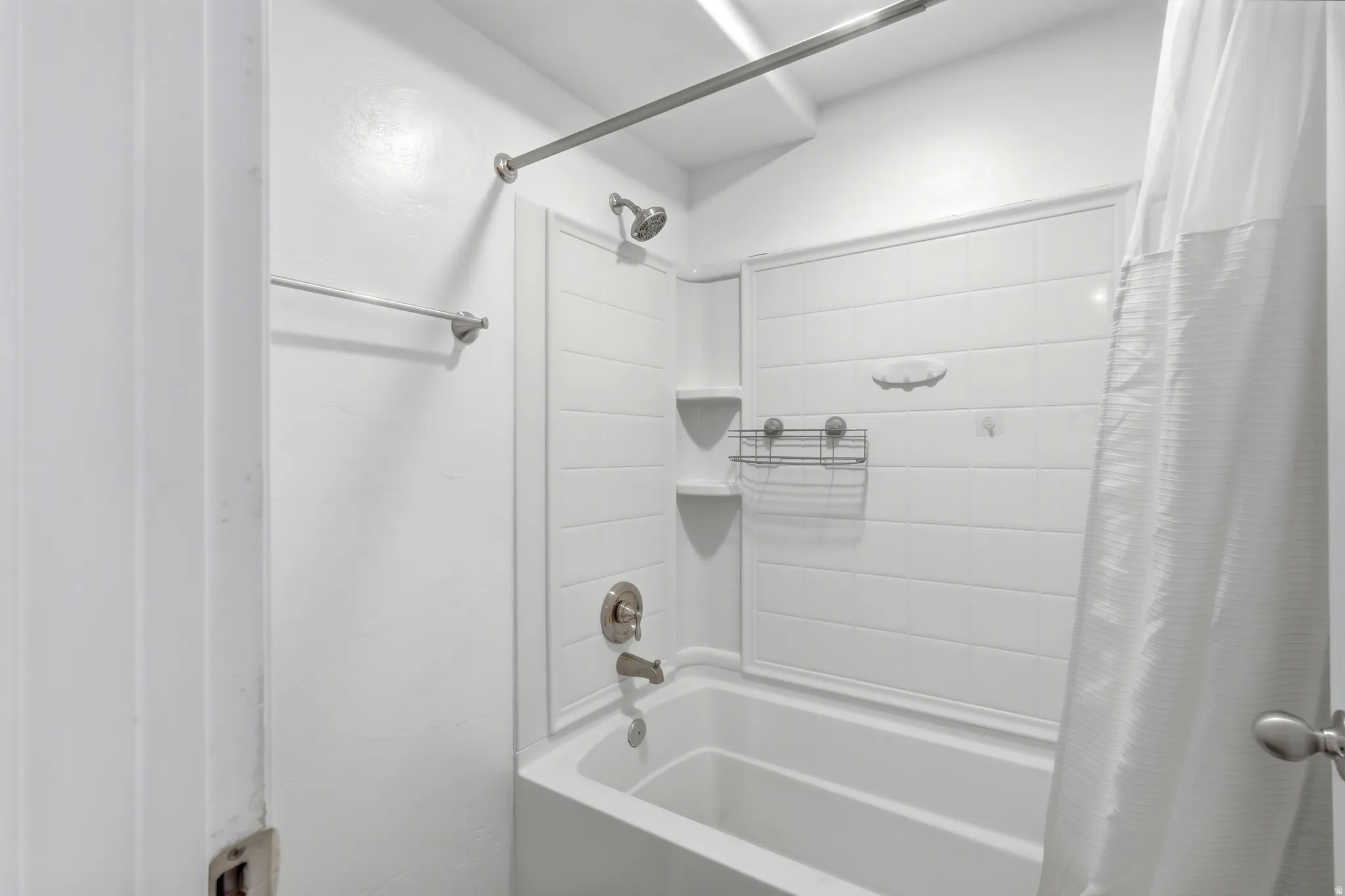 White-tiled bathtub and shower combination with brushed nickel fixtures
