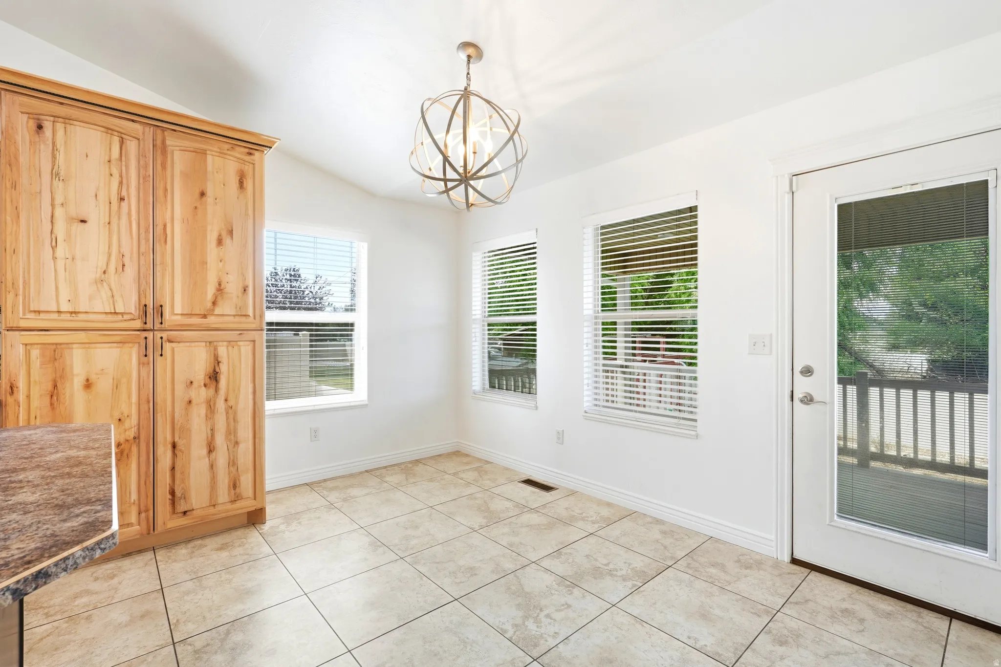 Spacious area featuring light-toned tile flooring, vaulted white ceilings, and a geometric chandelier