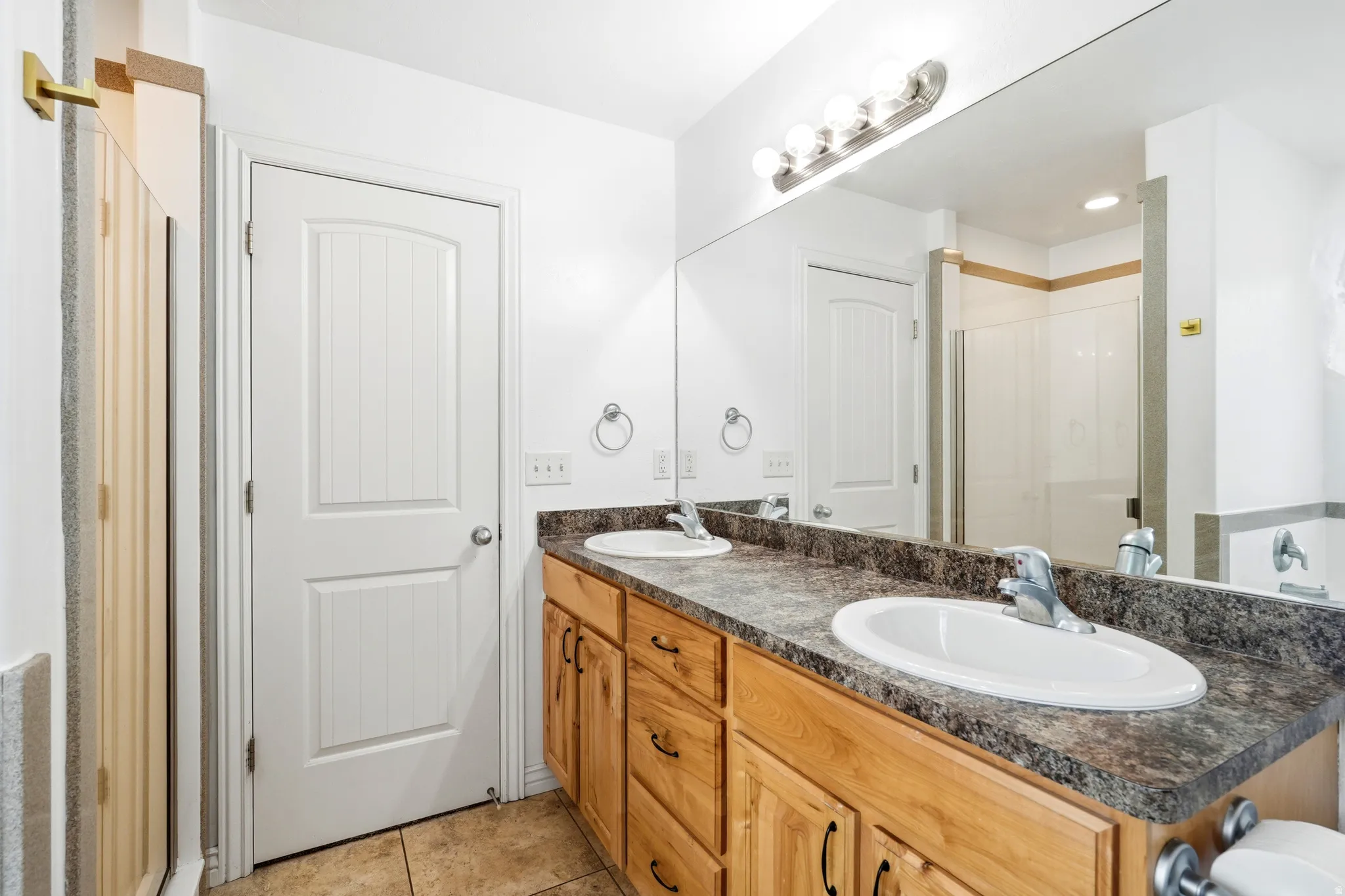Dual vanity with light wood cabinetry, stone-finish countertop, and undermount sinks