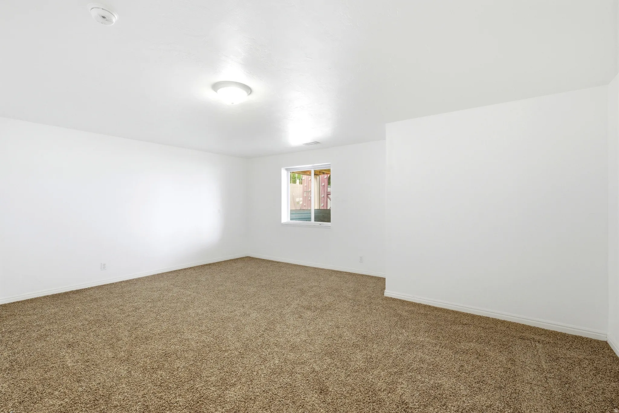 Spacious room featuring neutral carpeting, white walls, a single window, and overhead lighting