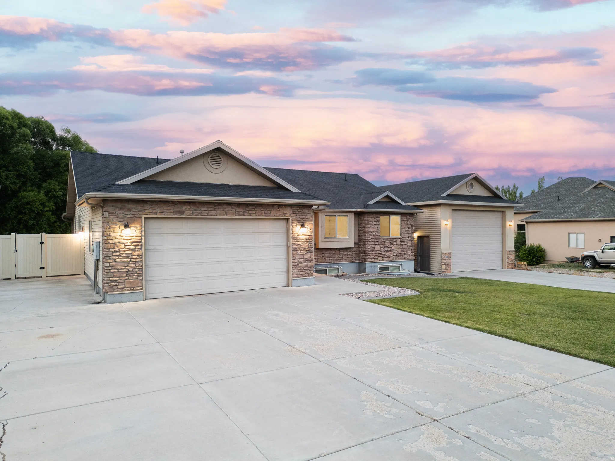 Exterior featuring stone veneer accents, two attached garages with overhead doors, a paved driveway, and manicured lawn