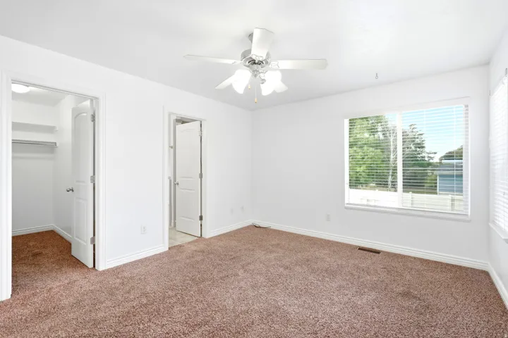 Spacious room featuring neutral carpeting, white walls, and a ceiling fan with integrated lighting