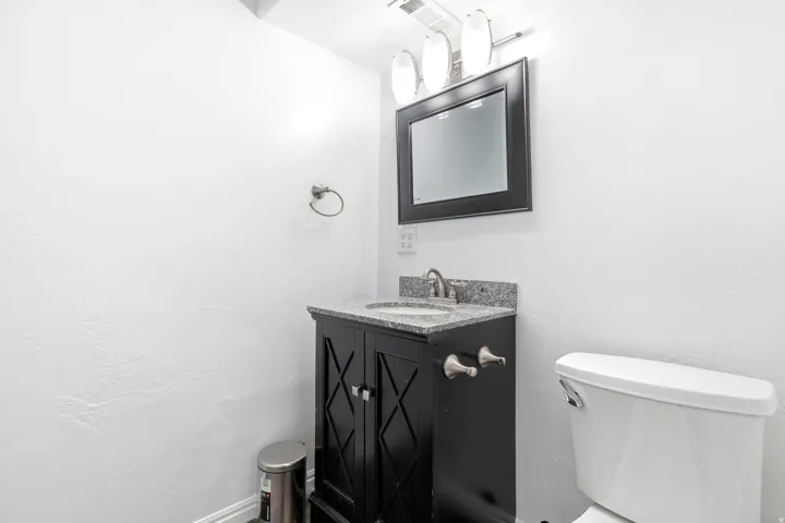 Powder room featuring a black vanity with crosshatch detailing, granite countertop, undermount sink, and framed mirror with a three-bulb vanity light