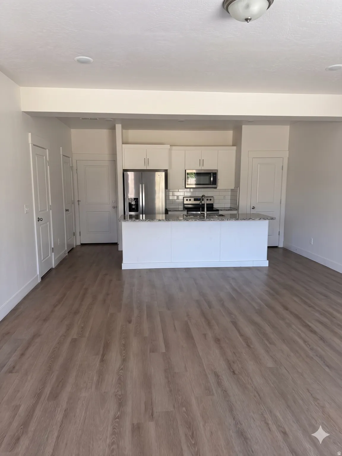 Open-concept living area featuring wood-finish flooring, white walls, and a modern kitchen