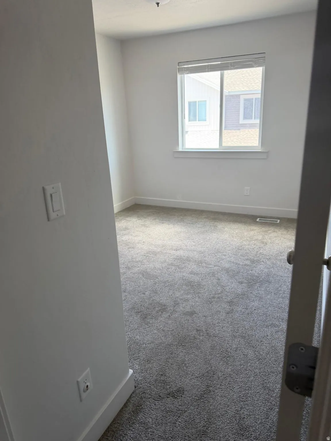 Carpeted room featuring a double-paned window with blinds, white trim throughout, and a flush-mount ceiling light