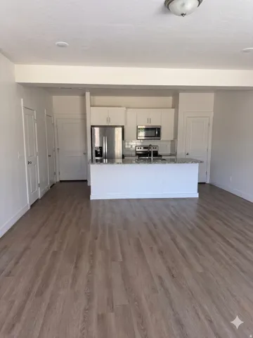 Open-concept living area featuring wood-finish flooring, white walls, and a modern kitchen