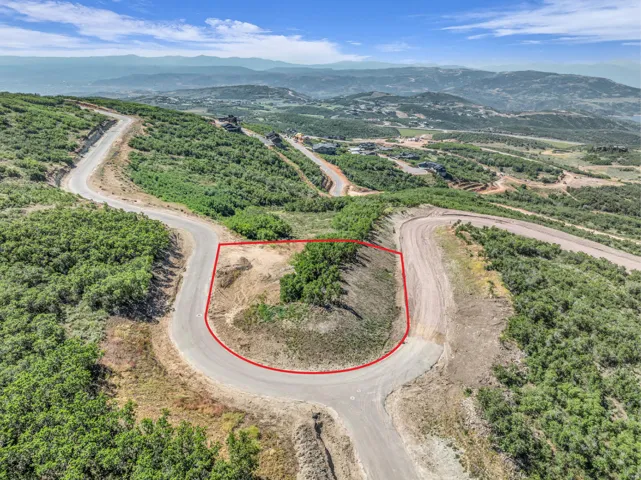 Mountainous landscape featuring a developed lot with winding roads, surrounding greenery, and distant structures