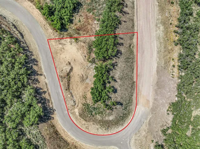Aerial view of a U-shaped property lot featuring a paved road frontage and natural terrain