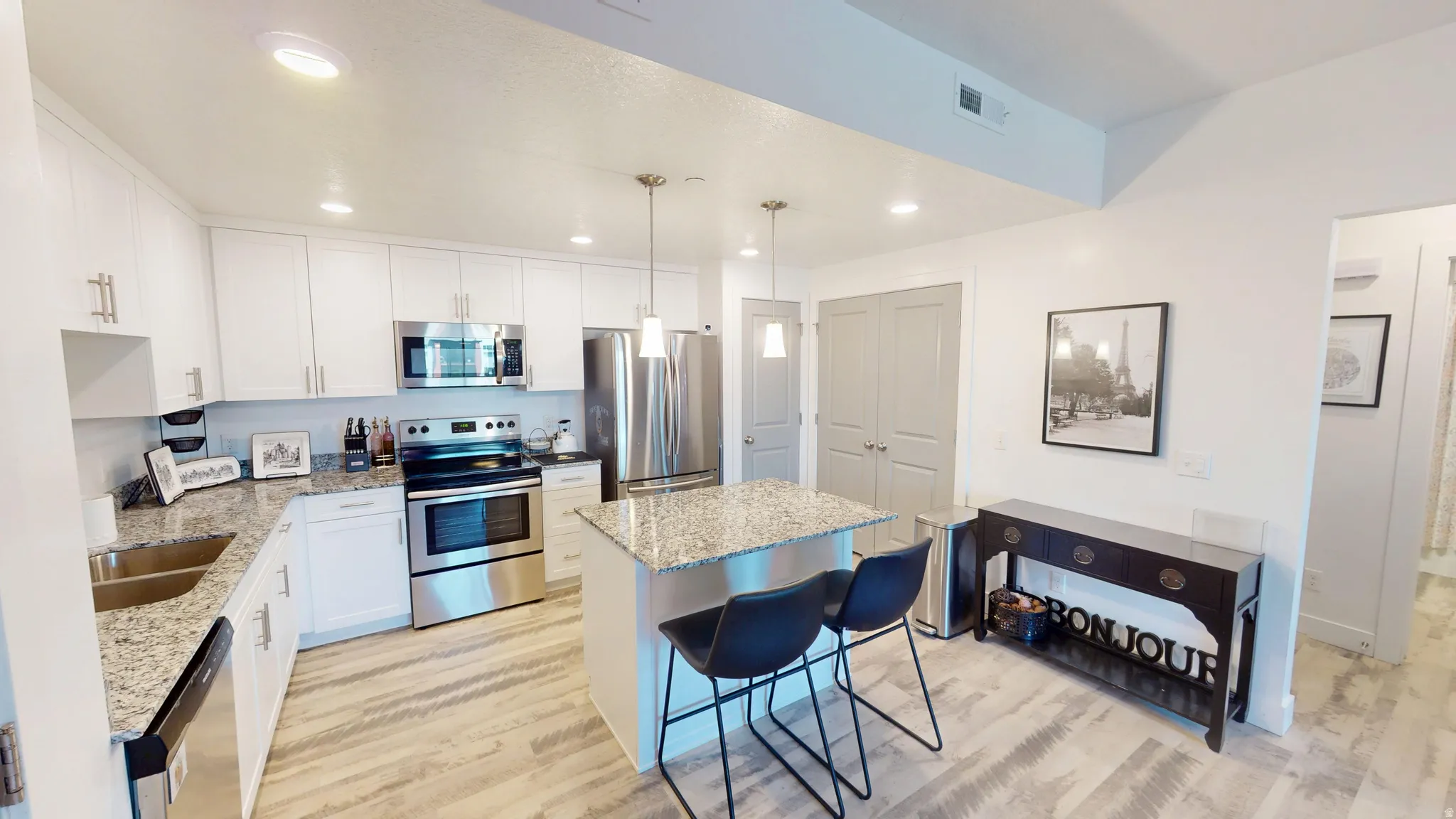 Kitchen featuring white cabinetry, stainless steel appliances, granite countertops, a central island with pendant lighting, and wood-finish flooring