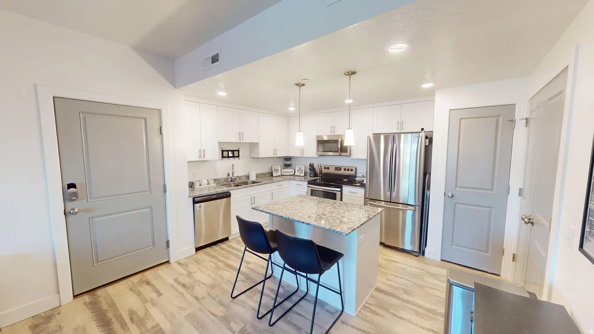 Contemporary kitchen featuring white cabinetry, stainless steel appliances, a center island with bar seating, pendant lighting, and wood-finish flooring
