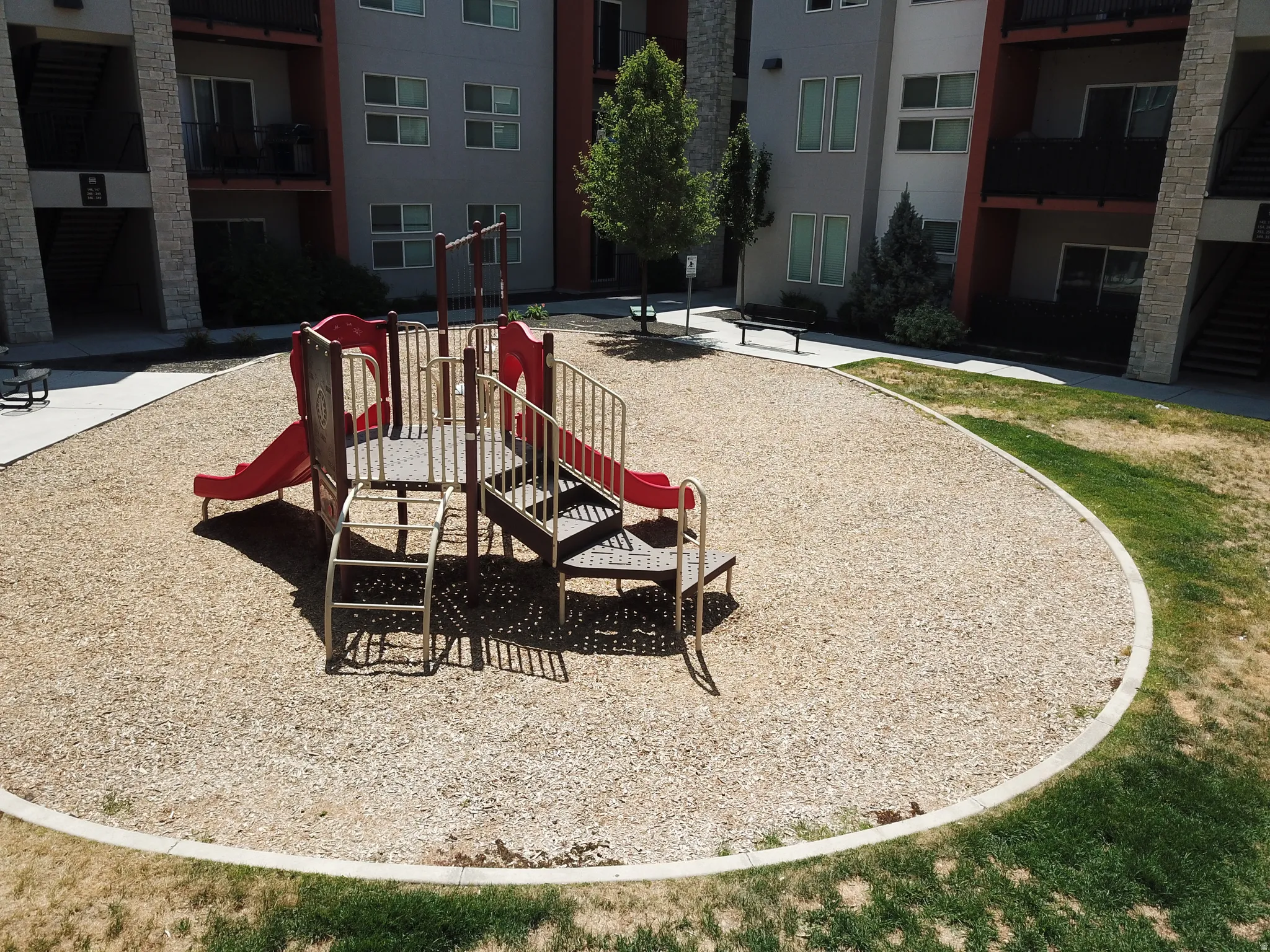 Outdoor playground featuring a red and brown play structure with slides and climbing elements, surrounded by wood chip surfacing