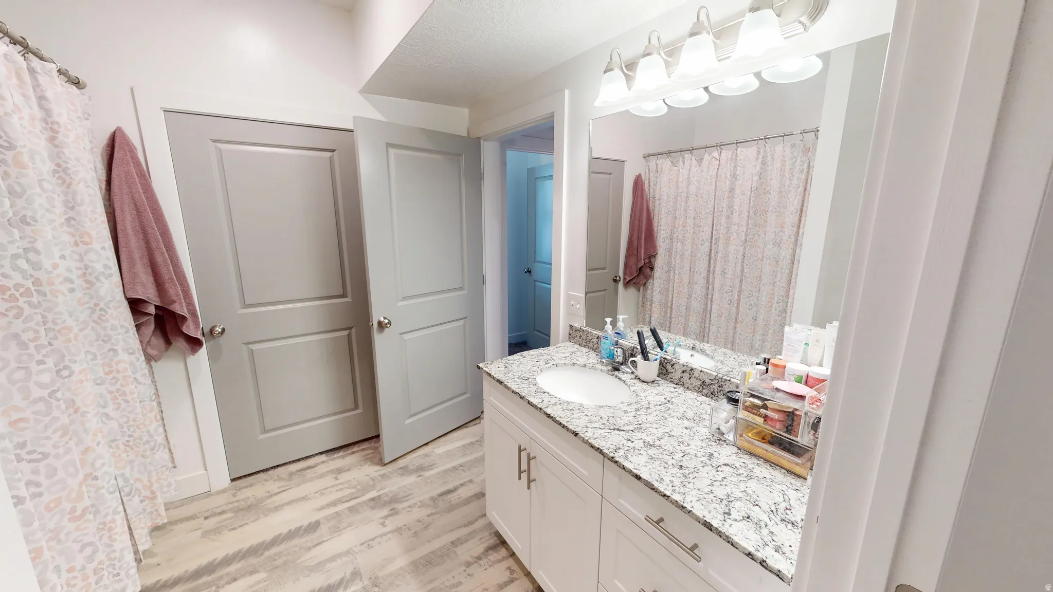 Bathroom featuring a single vanity with stone-finish countertop, white cabinetry, and a framed mirror