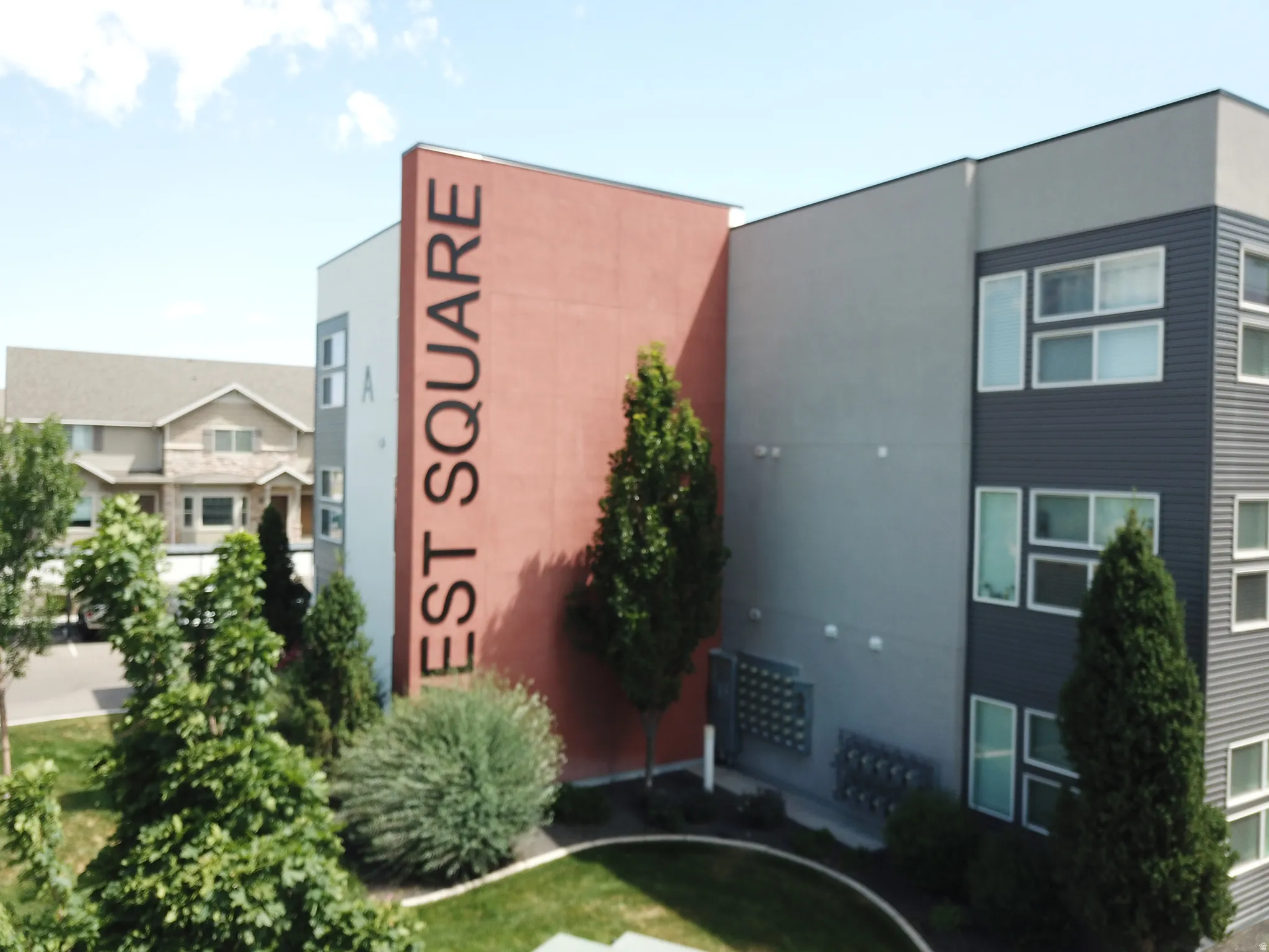Modern multi-story building featuring a red-orange facade with prominent signage, grey and white exterior panels, and dark siding with multiple windows
