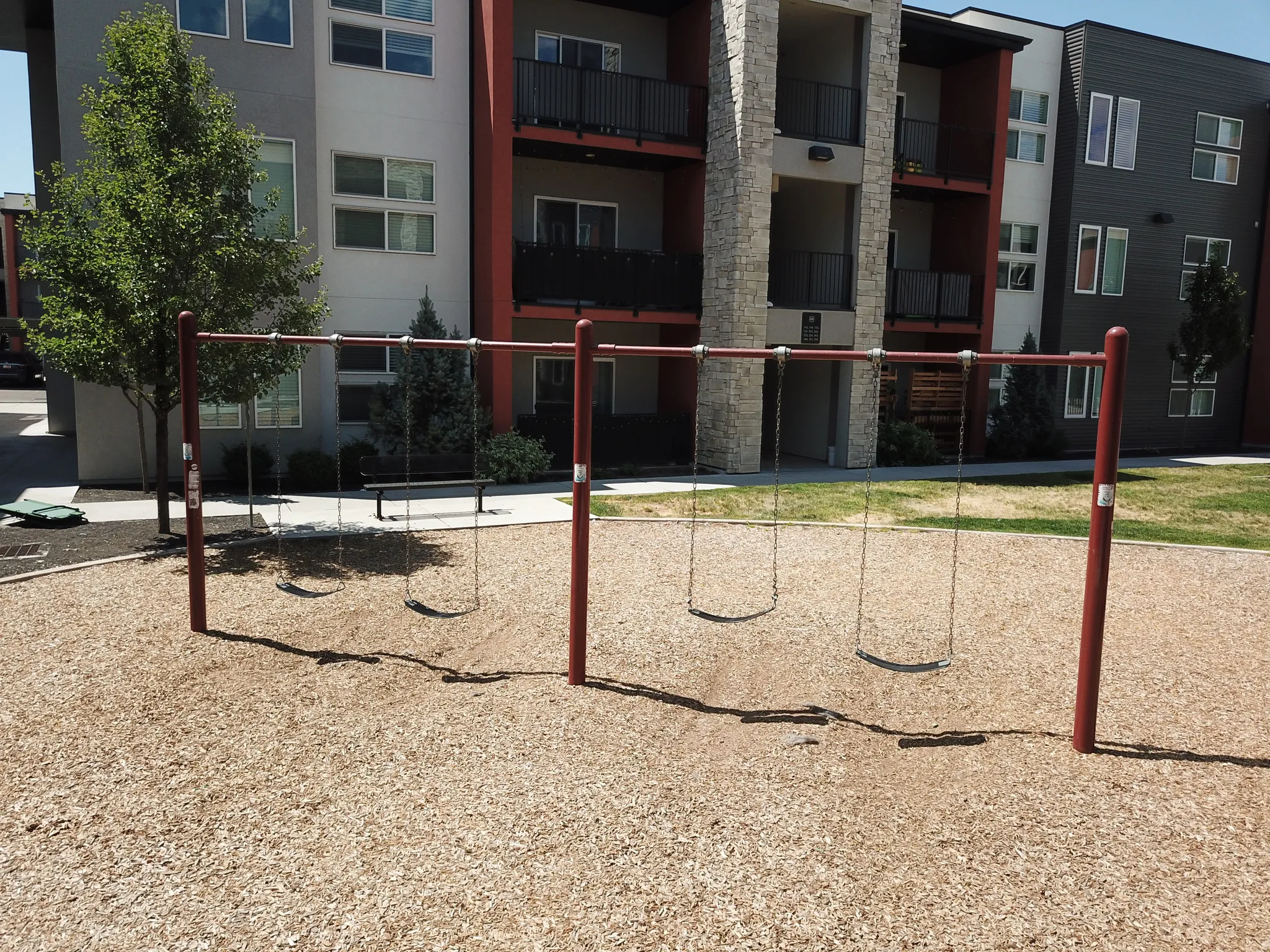 Outdoor play area featuring a swing set with four swings, set over wood chip surfacing