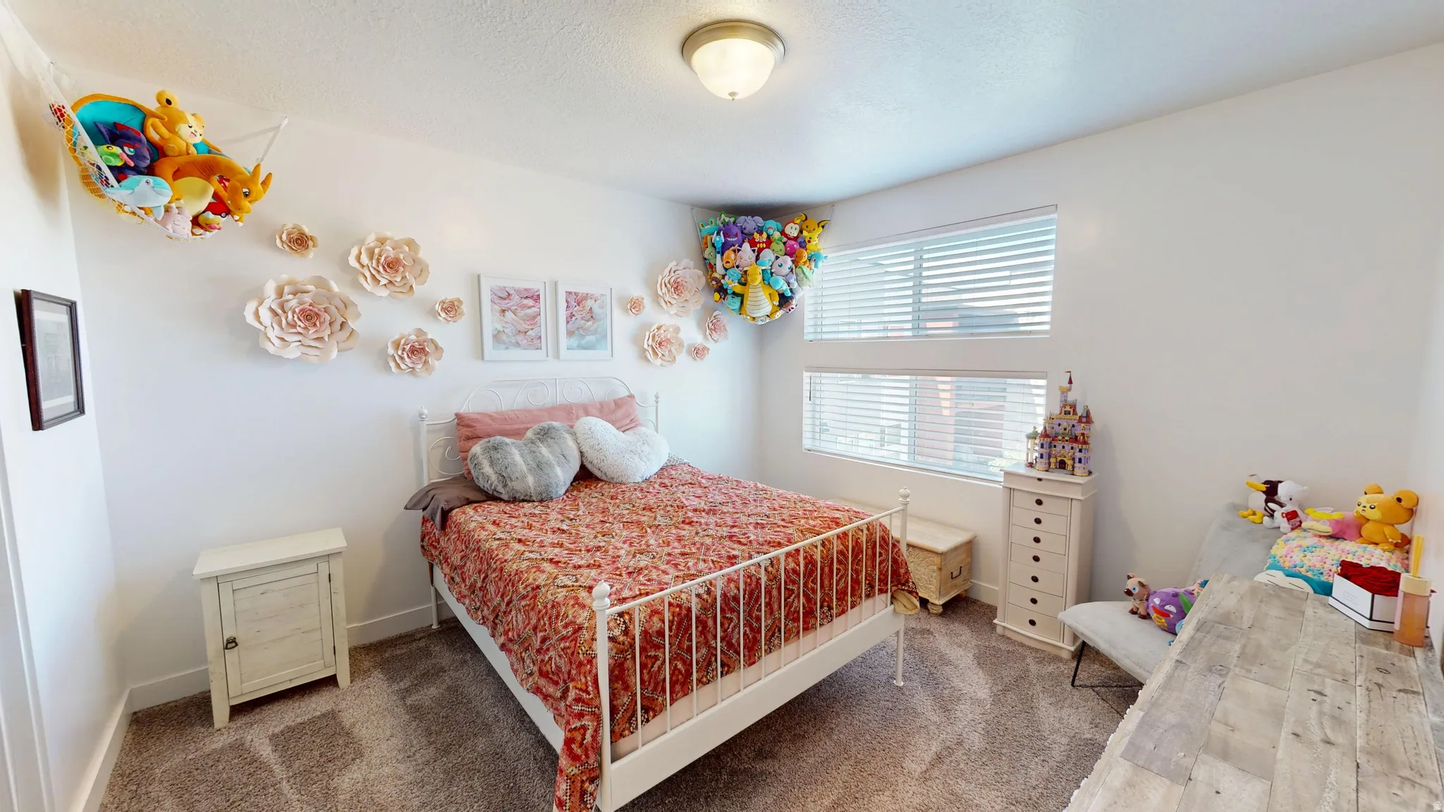 Carpeted bedroom featuring multiple windows with blinds, a white metal bed frame, and a ceiling-mounted light fixture