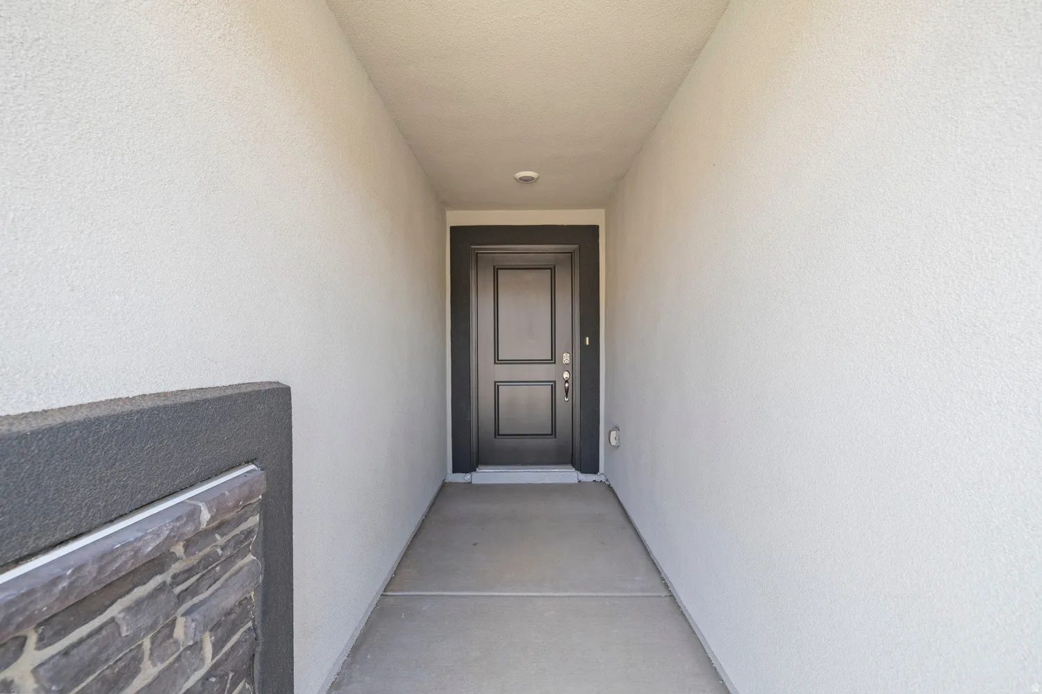 Entryway featuring a paneled door with dark trim, textured stucco walls, and a stone accent partition
