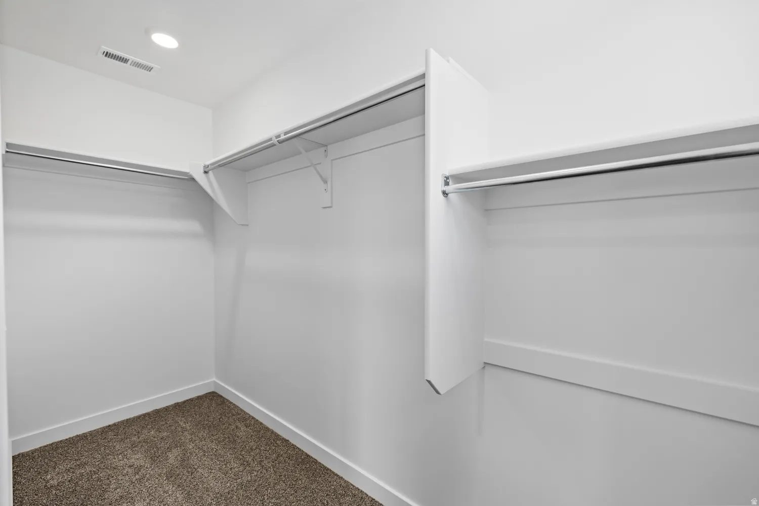 Walk-in closet featuring white walls, deep brown carpet flooring, and a recessed ceiling light