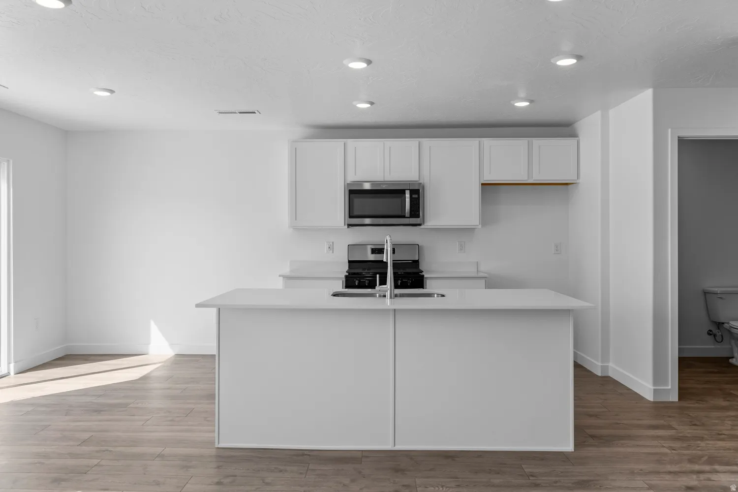 Contemporary kitchen featuring a large island with an undermount sink and chrome faucet, white cabinetry, a built-in microwave, and stainless steel range