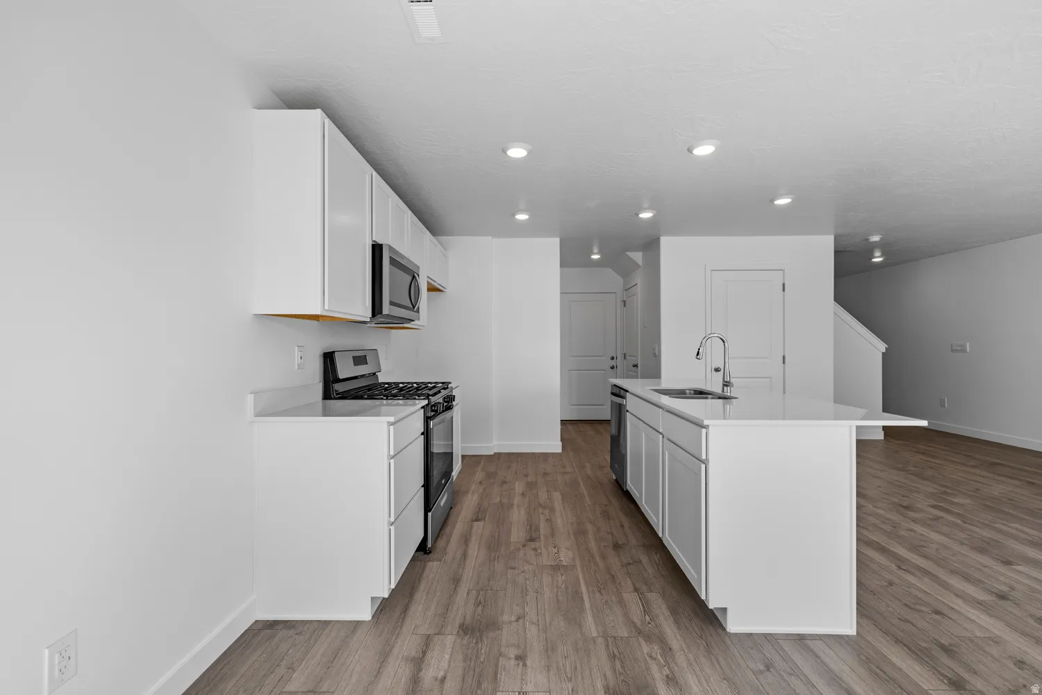 Contemporary kitchen featuring white cabinetry, stainless steel appliances, and a central island with an integrated sink