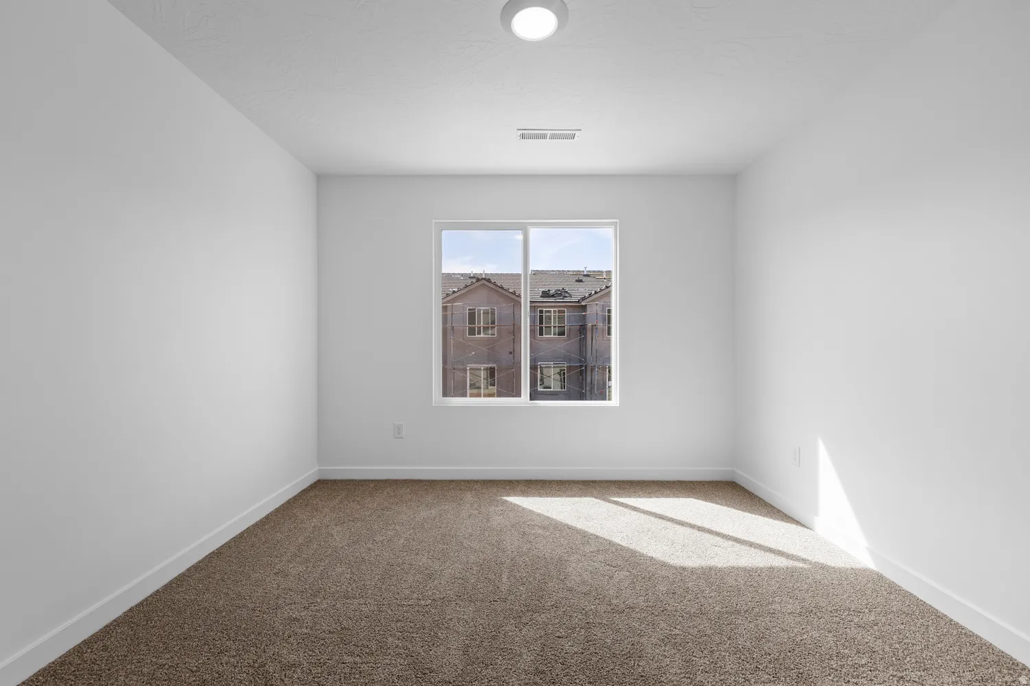 Bright room featuring a single window, neutral-tone carpeting, white baseboards, a white ceiling with a flush-mount light fixture, and a ceiling vent