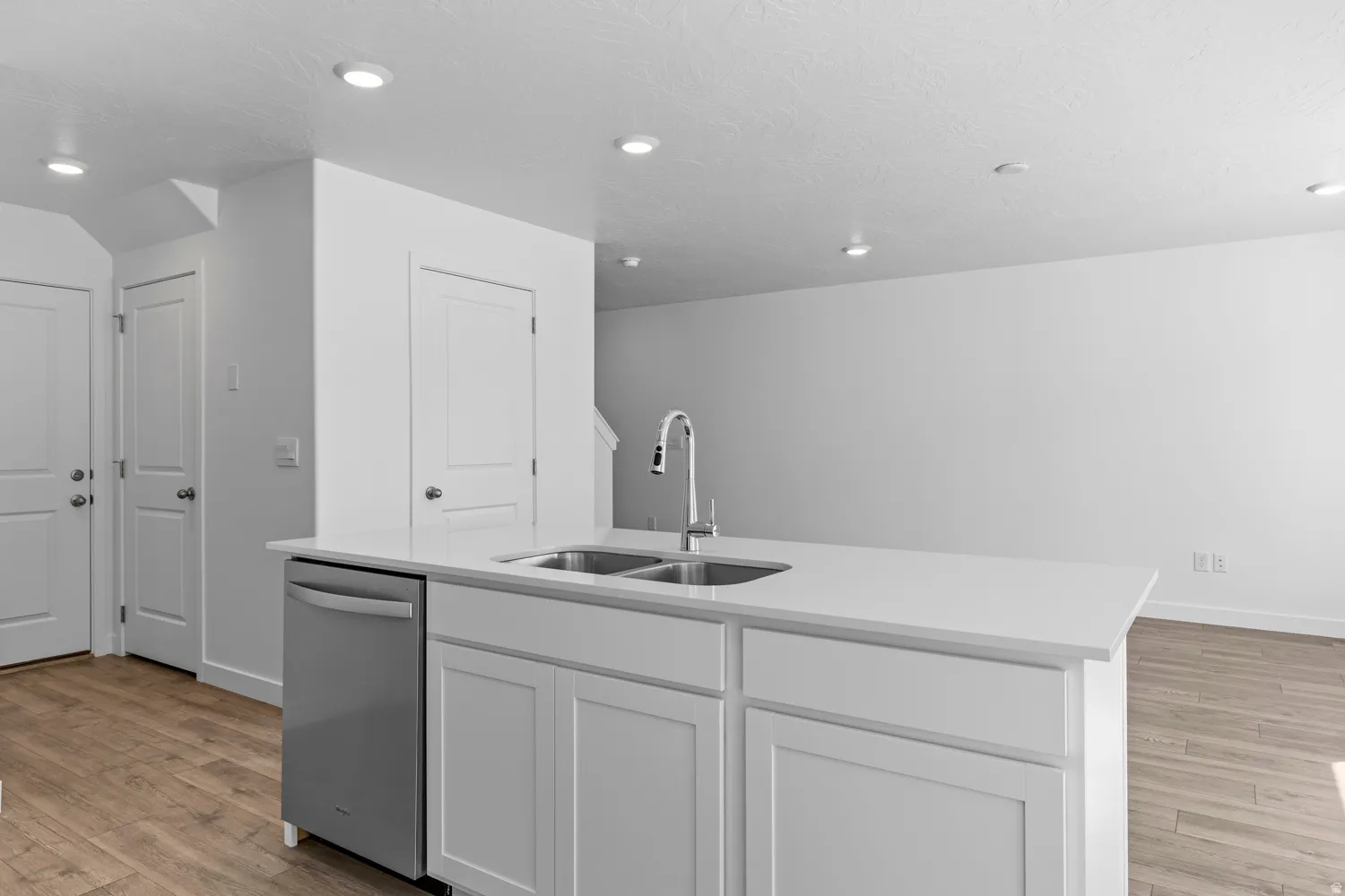 Kitchen island featuring a double-basin stainless steel sink with a high-arc faucet, integrated dishwasher, white shaker-style cabinetry, and a light-toned countertop