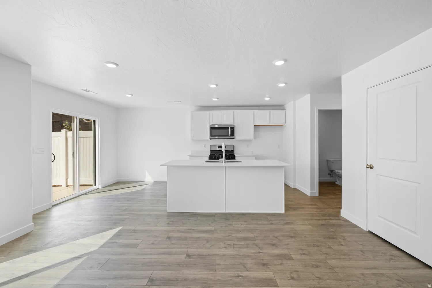 Open-concept living area featuring wood-finish flooring, recessed lighting, and a sliding glass door to an outdoor patio with privacy fencing
