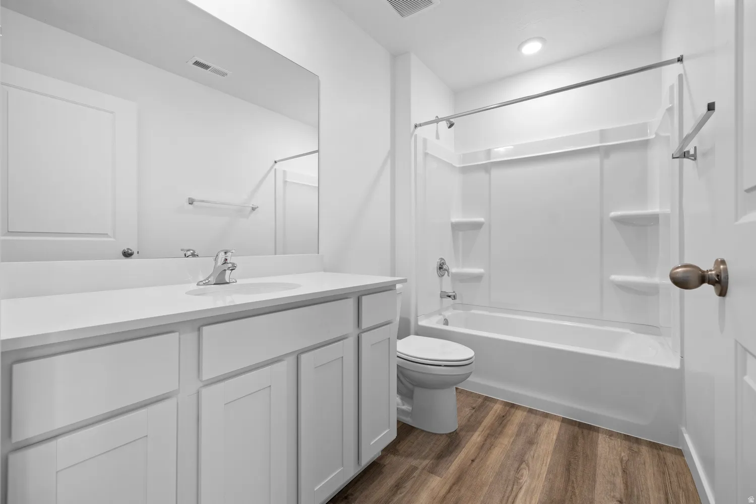 Modern full bathroom featuring a tub/shower combination with a white surround, a white vanity with an integrated sink, a large wall-mounted mirror, and wood-finish flooring