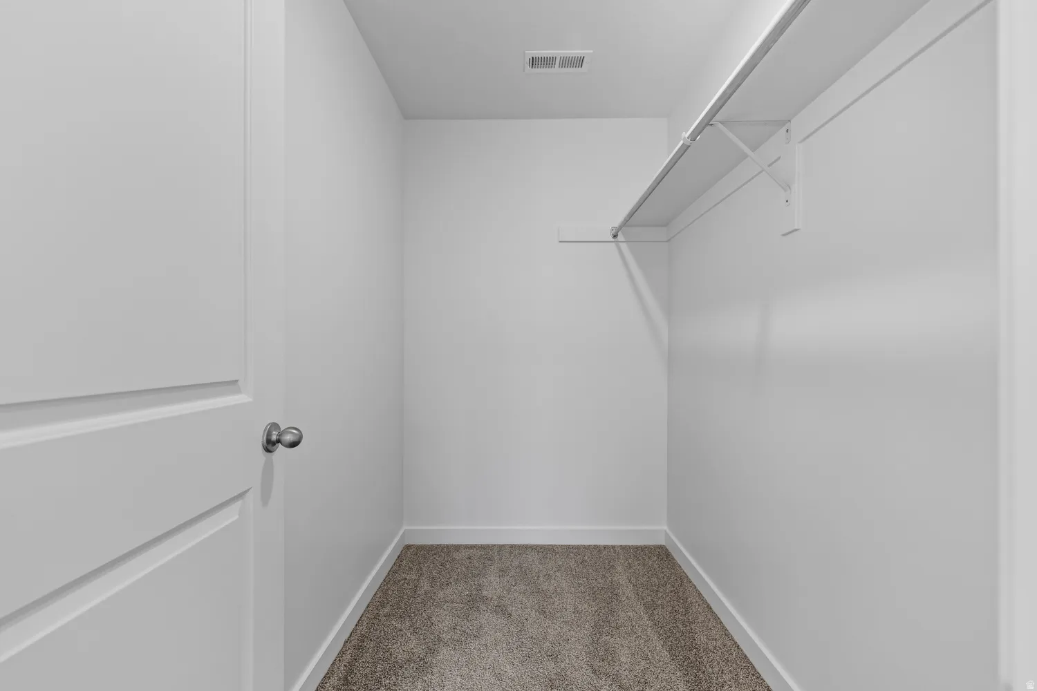 Spacious closet featuring white walls, gray carpet flooring, white baseboards, and built-in shelving with a hanging rod
