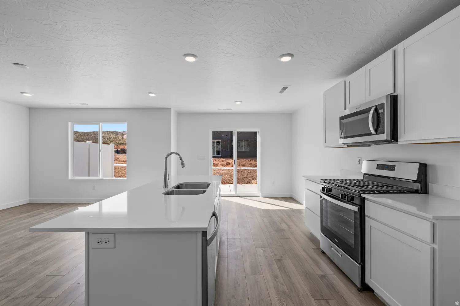 Open-concept kitchen featuring a large island with an undermount double sink, stainless steel appliances, light wood-finish flooring, and recessed lighting