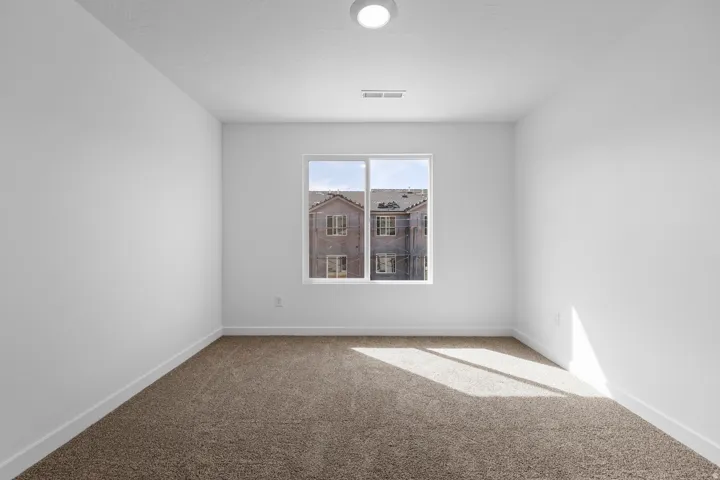 Bright room featuring a single window, neutral-tone carpeting, white baseboards, a white ceiling with a flush-mount light fixture, and a ceiling vent