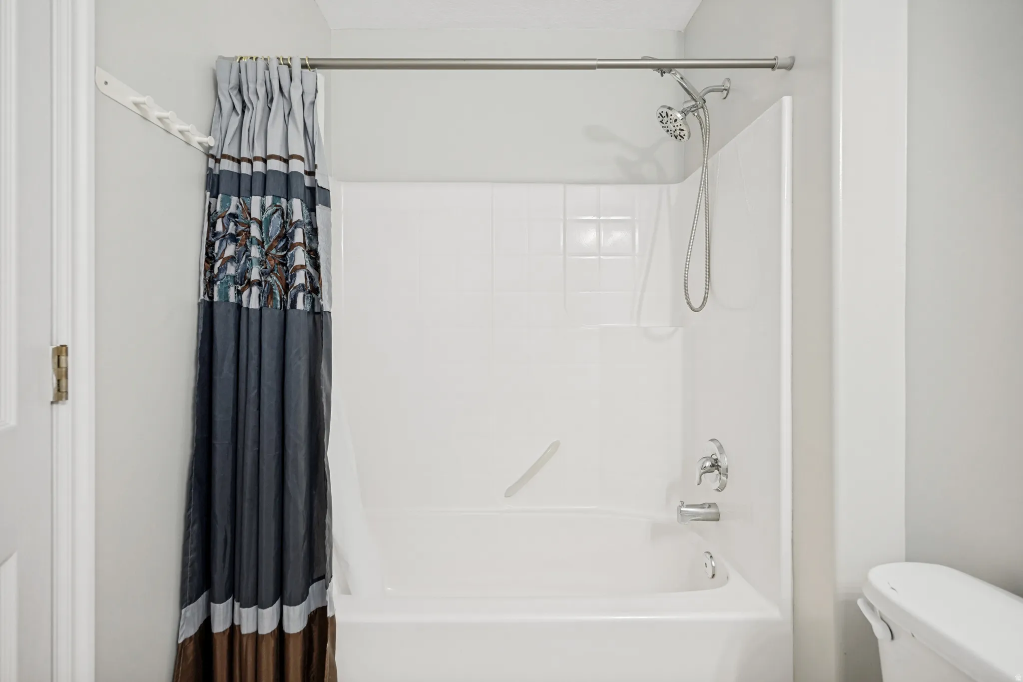 White acrylic bathtub and shower combination with chrome fixtures, including a showerhead with handheld sprayer