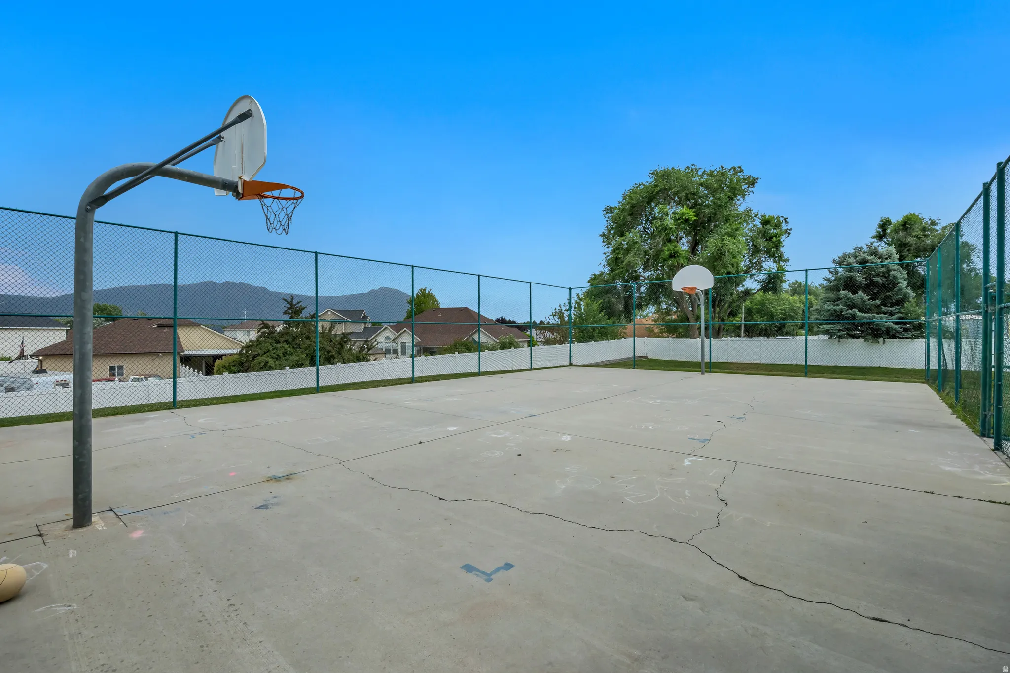 Outdoor sports court featuring two basketball hoops, chain-link fencing, and a concrete playing surface