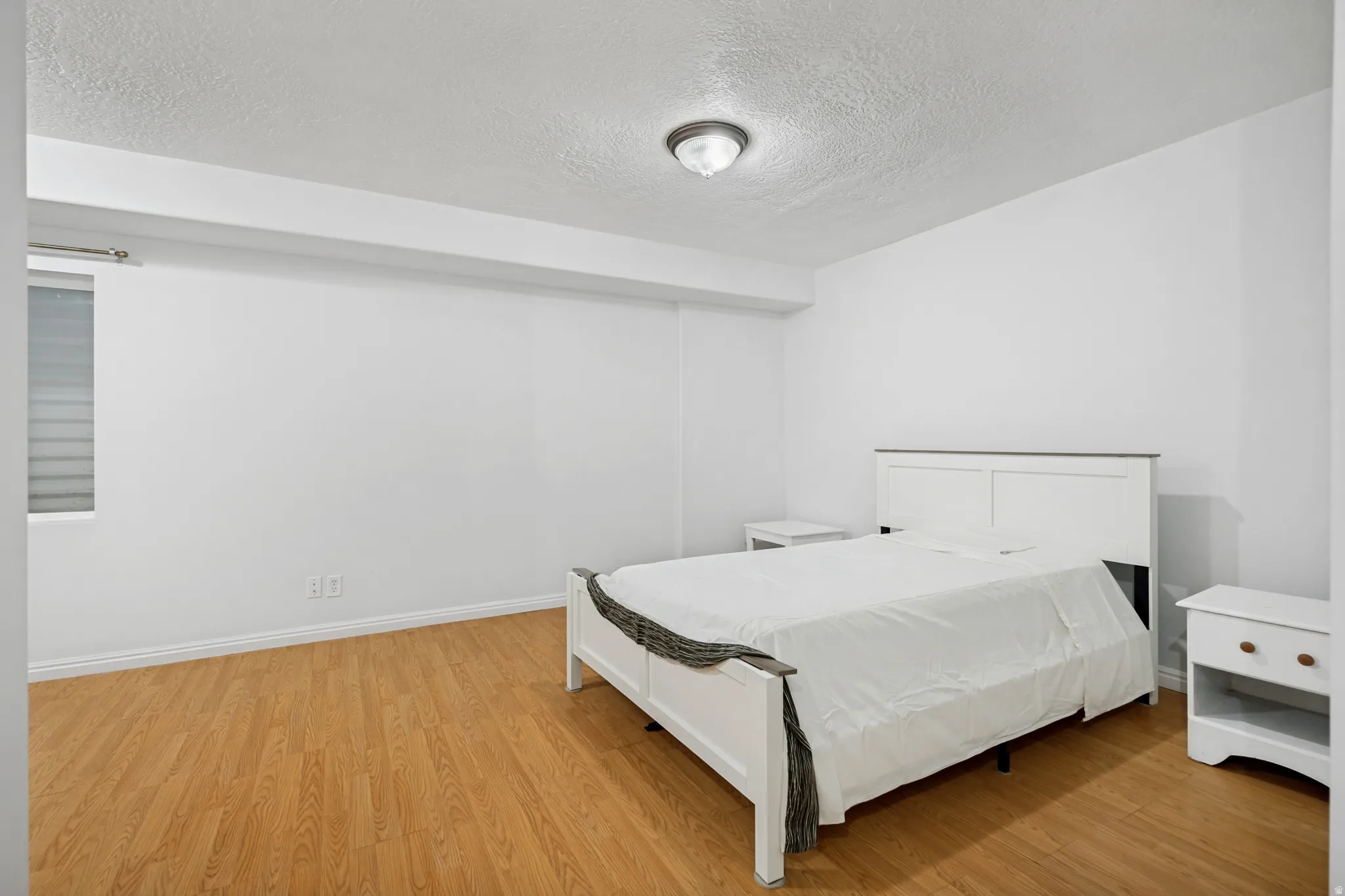 Bedroom featuring wood-finish flooring, white baseboards, a window with horizontal blinds, and a flush mount ceiling light