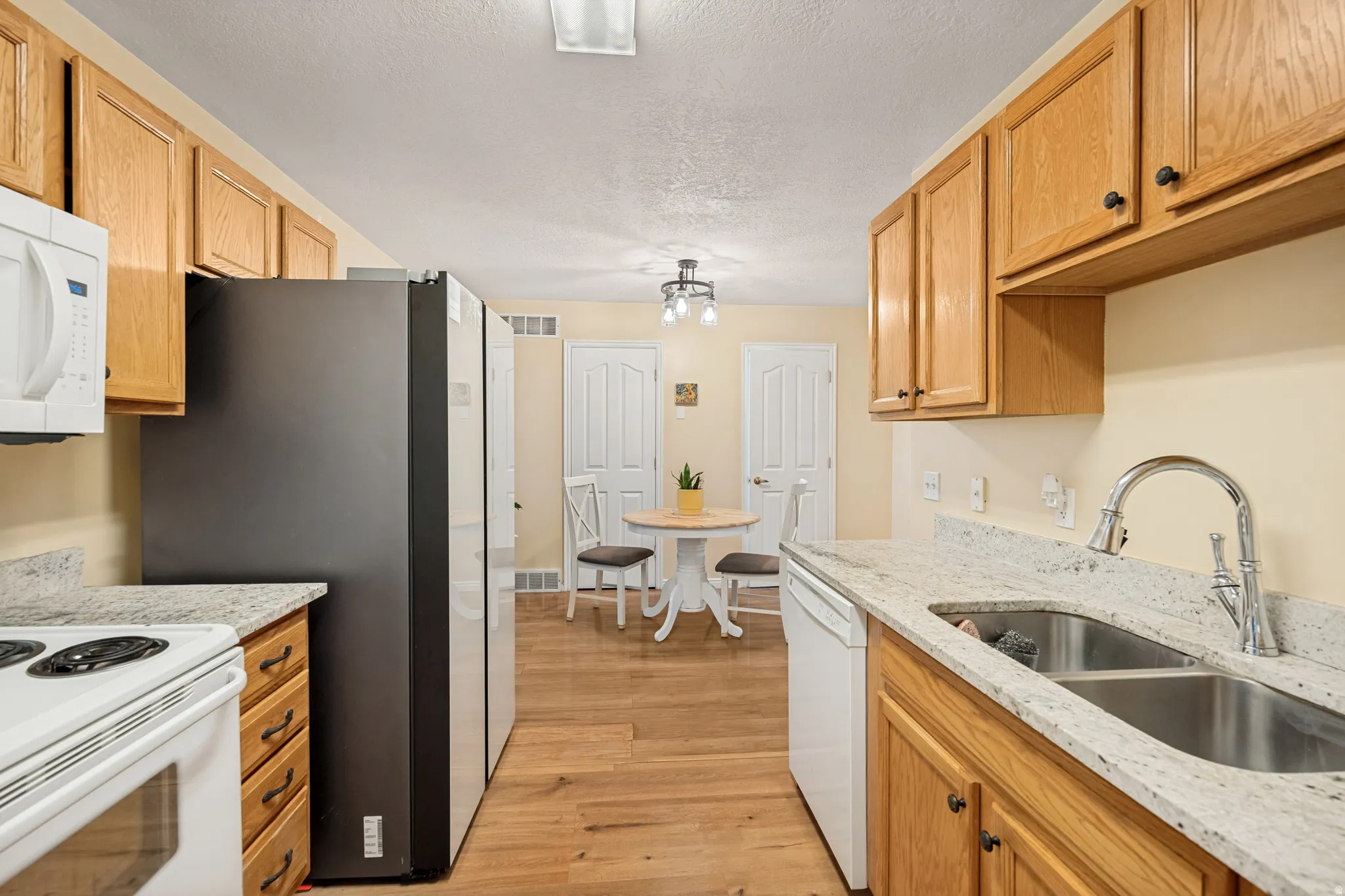 Kitchen featuring wood-finish flooring, light wood cabinetry, white countertops, and a double basin sink with a high-arc faucet
