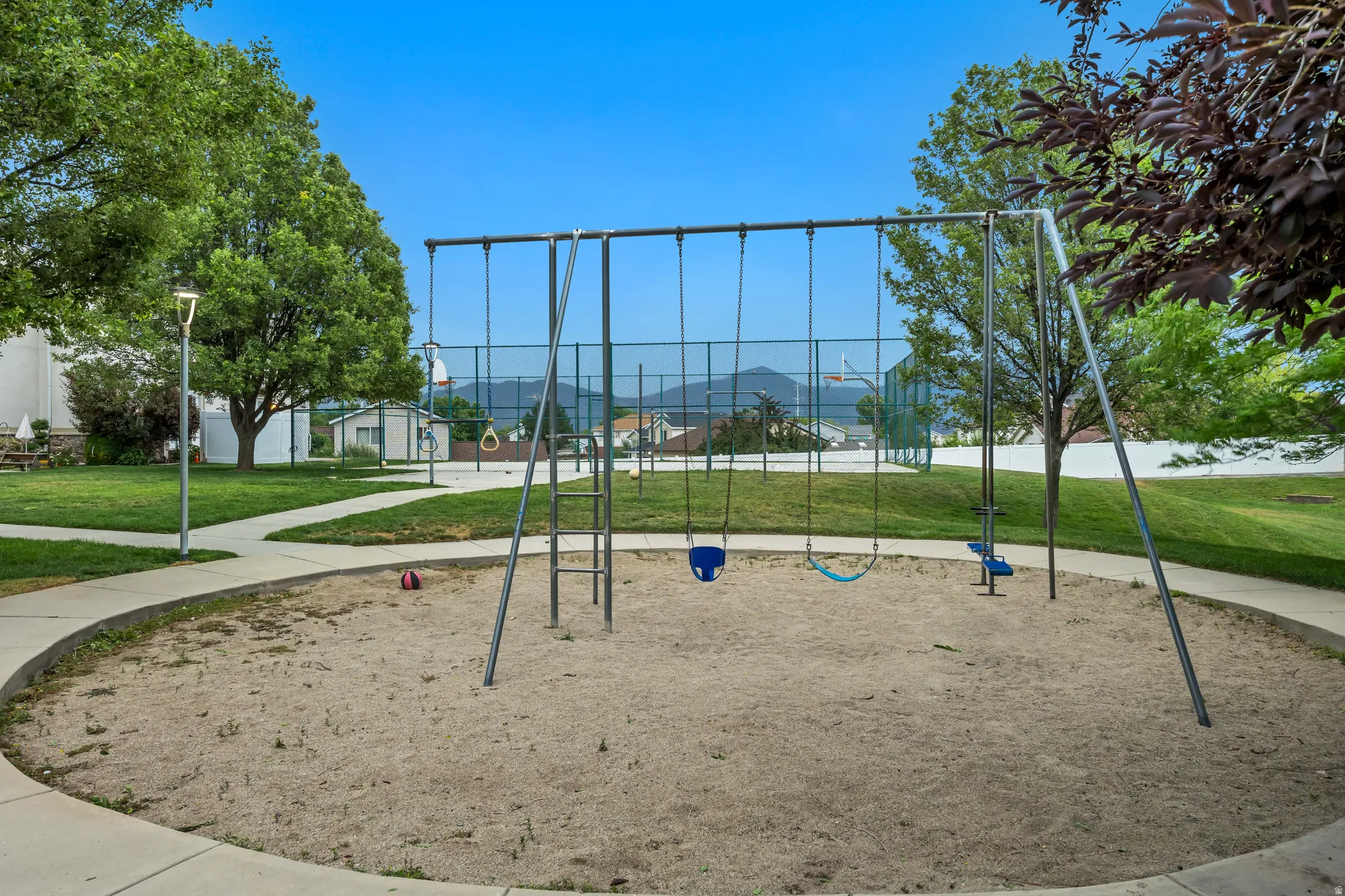 Community playground featuring a metal swing set, sand play area, and surrounding paved walkways