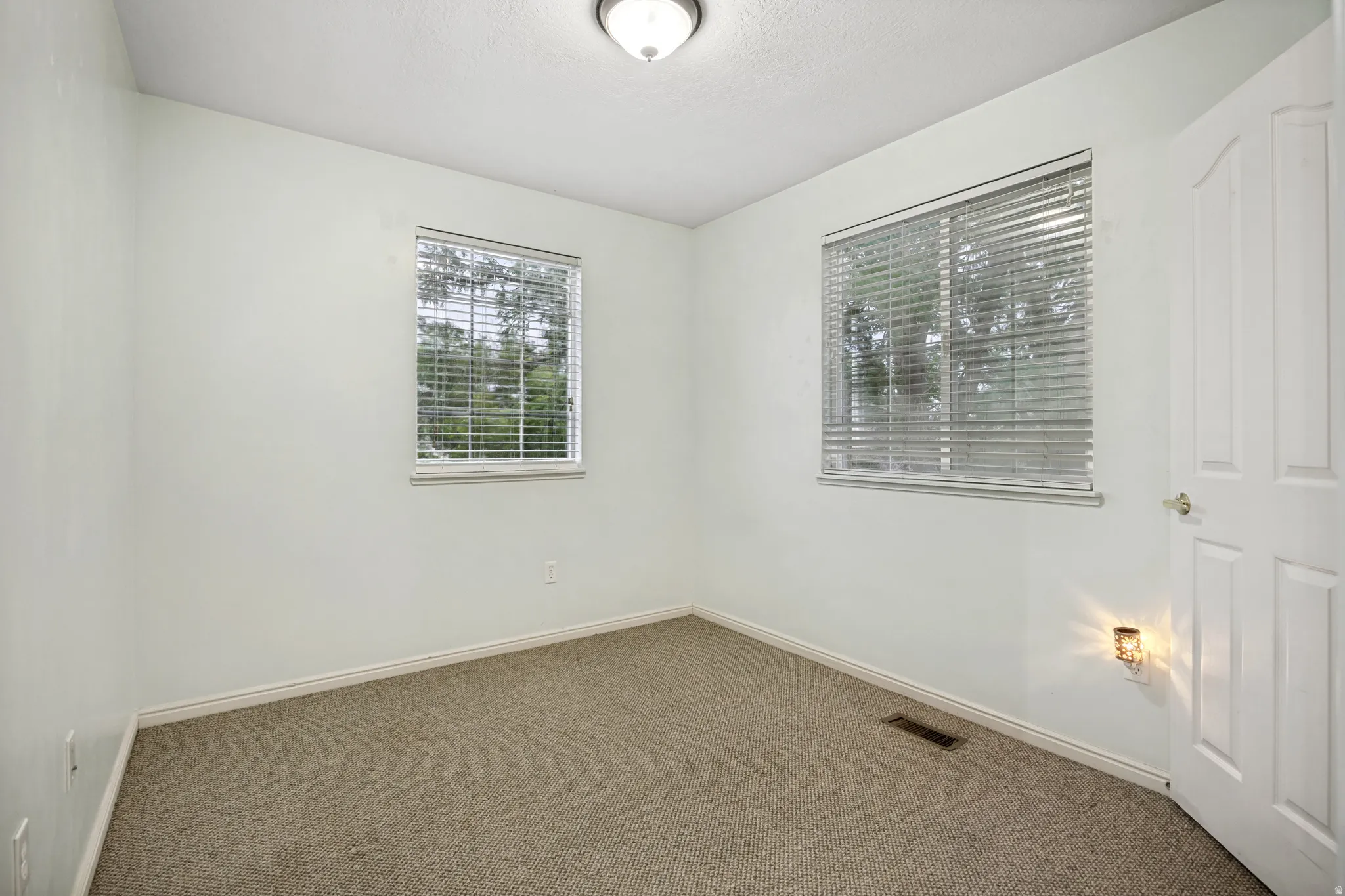 Bright room featuring two windows with blinds, neutral carpeting, and white walls