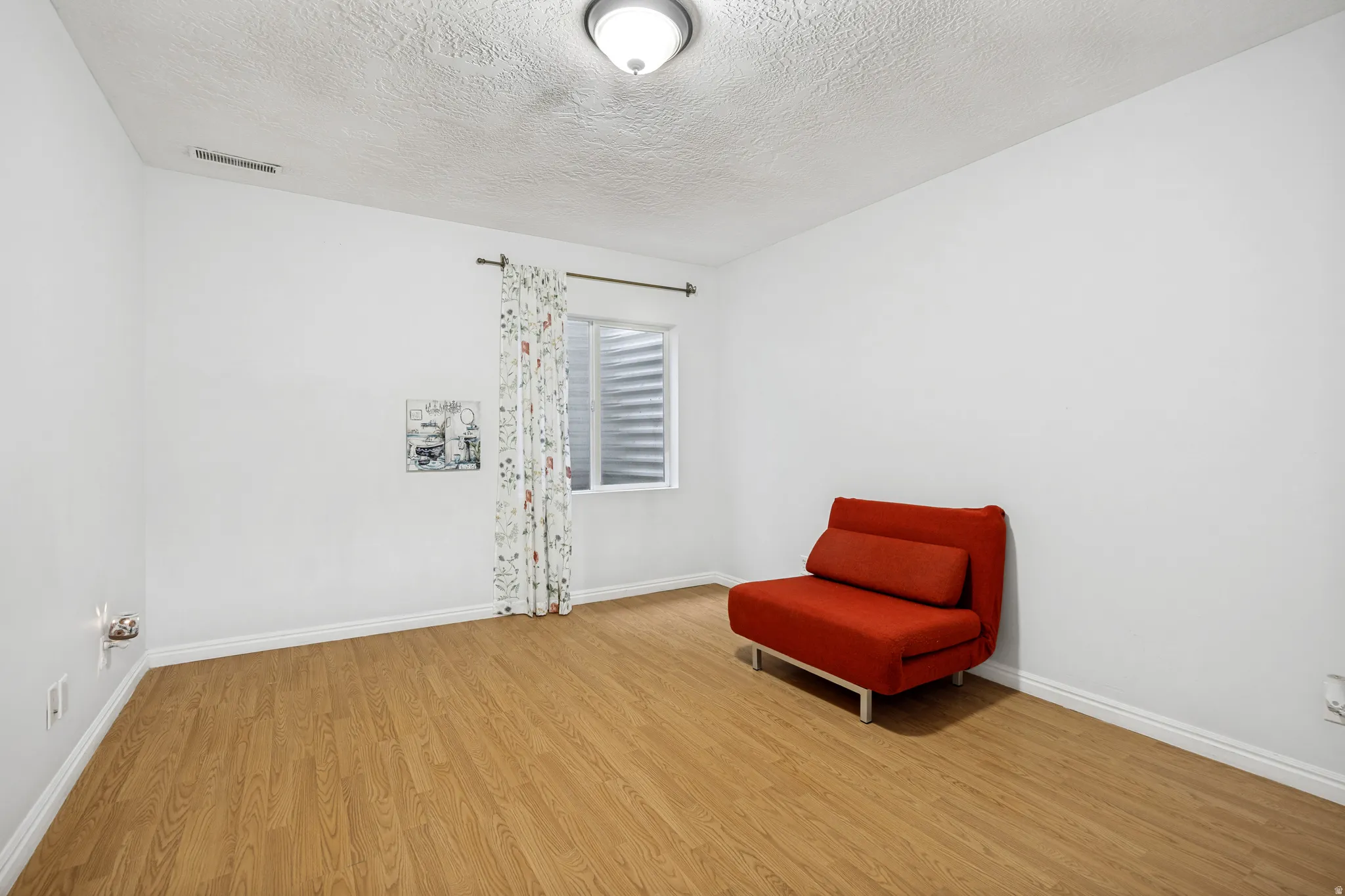 Spacious room featuring wood-finish flooring, white baseboards, and a window with a security grate