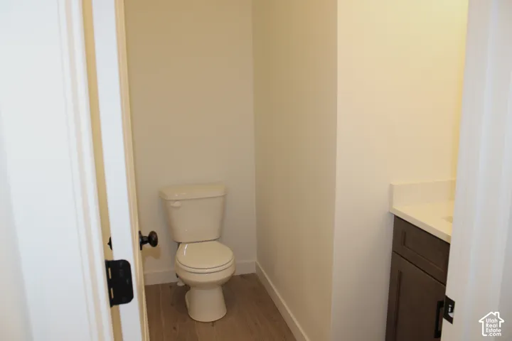 Compact bathroom space featuring a neutral tone toilet, wood-finish flooring, a dark wood-finish vanity, and a light-colored countertop