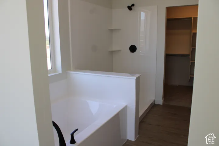 Soaking tub featuring a matte black faucet, a separate shower with black fixtures and built-in shelving, a window, and wood-finish flooring