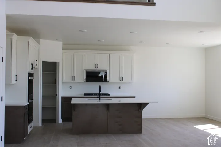 Modern kitchen featuring white upper cabinetry, dark base cabinetry, and a central island with a light-toned countertop
