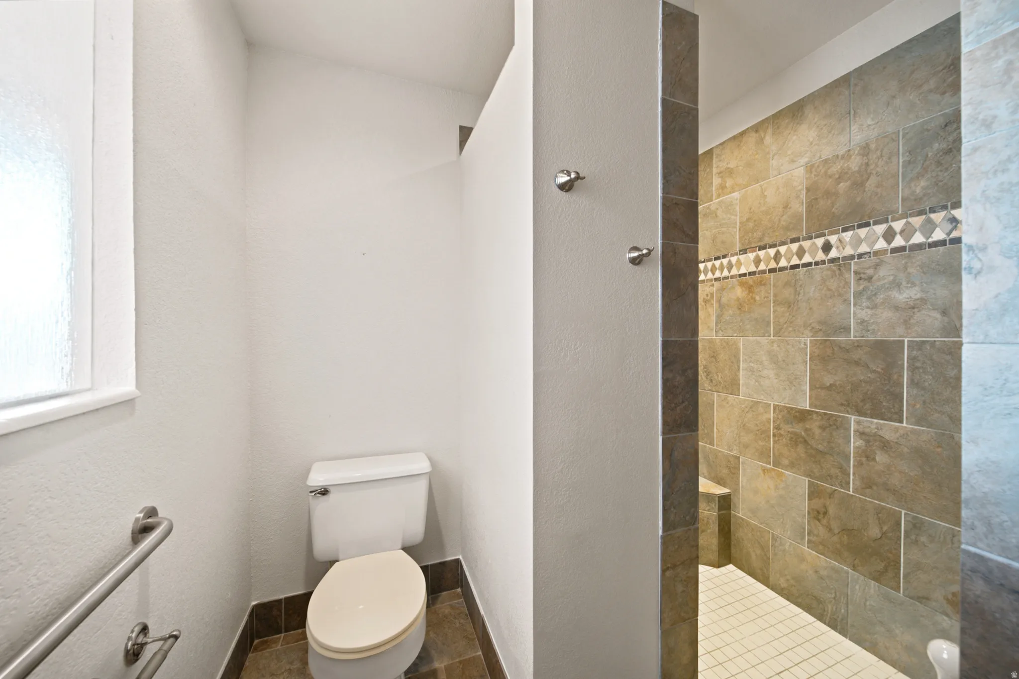Tiled shower with decorative accent band and built-in bench, complemented by a white toilet and frosted window
