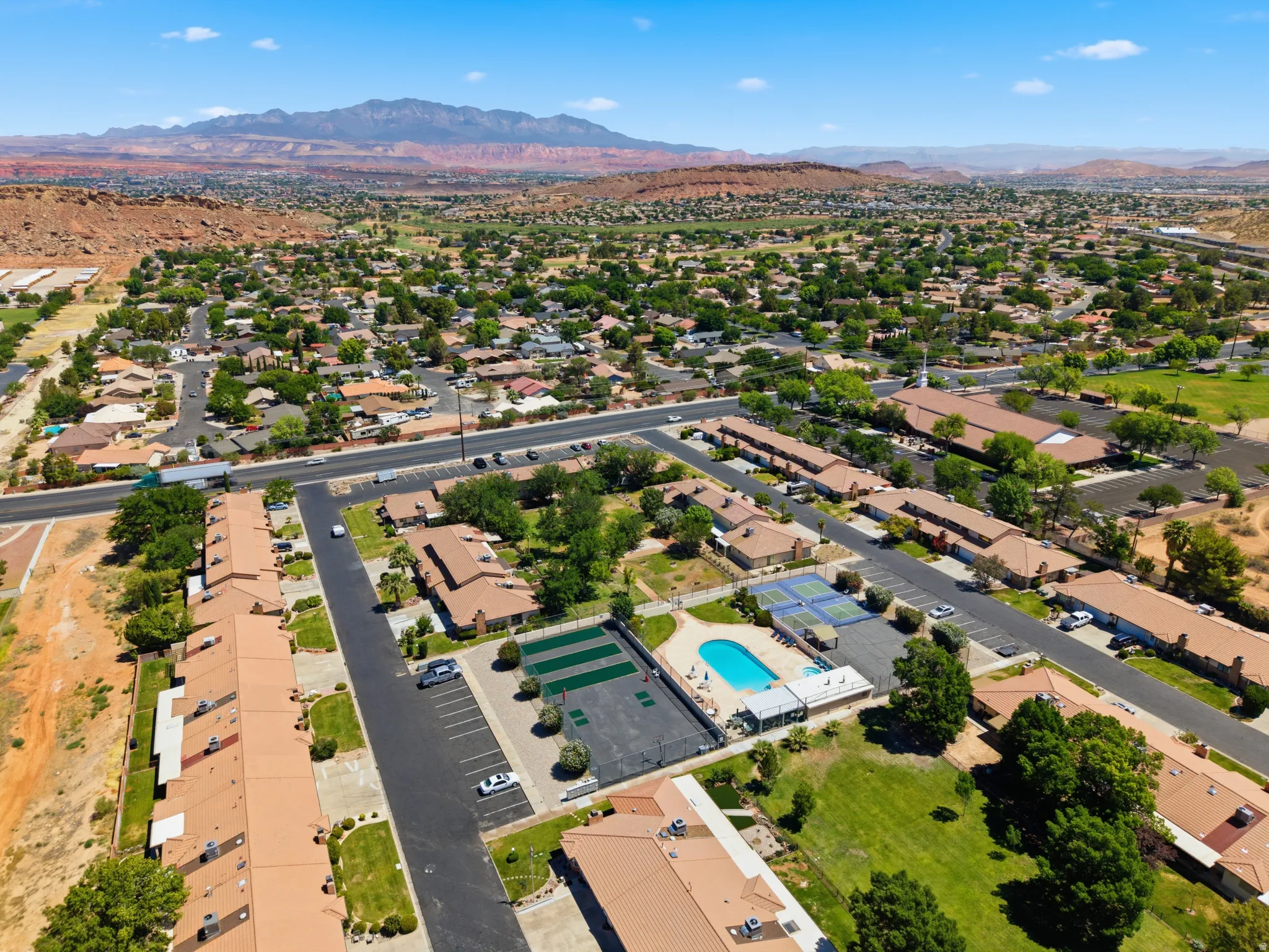 Aerial perspective showcasing the community layout with residential structures, extensive green spaces, a swimming pool, and tennis courts