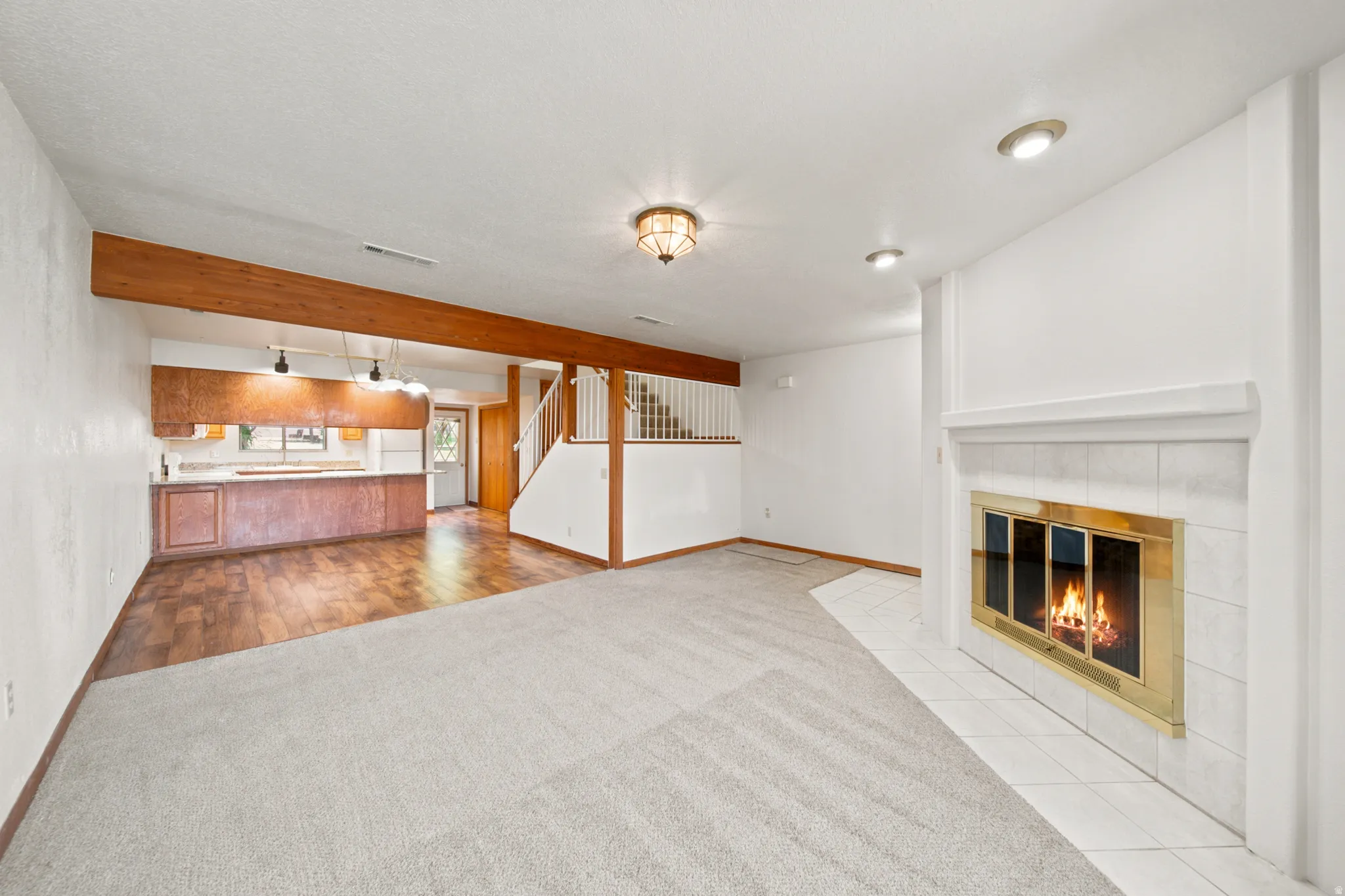 Open-concept living area featuring a tile-surround fireplace with a brass insert, recessed lighting, and a wood-finish flooring section