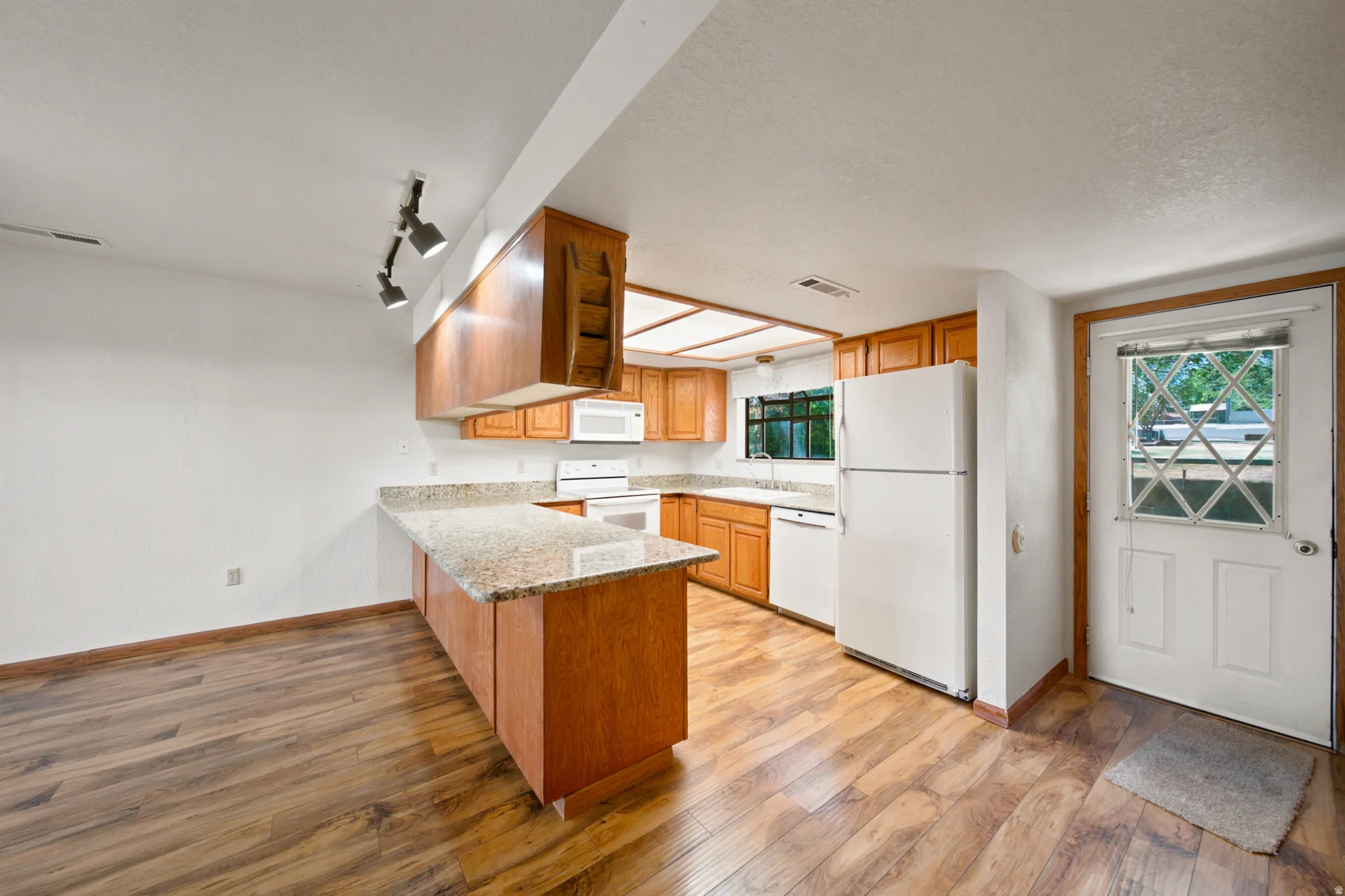 Kitchen featuring wood-finish flooring, wood cabinetry, stone countertops, and white appliances