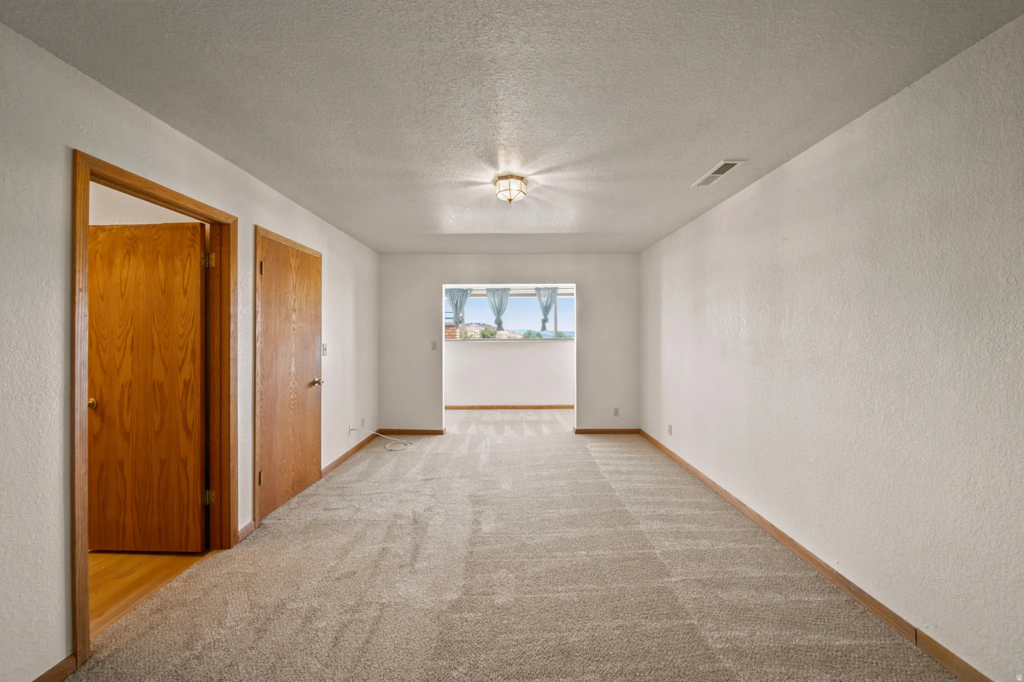 Spacious room featuring neutral carpet flooring, white walls, and wood-finish trim