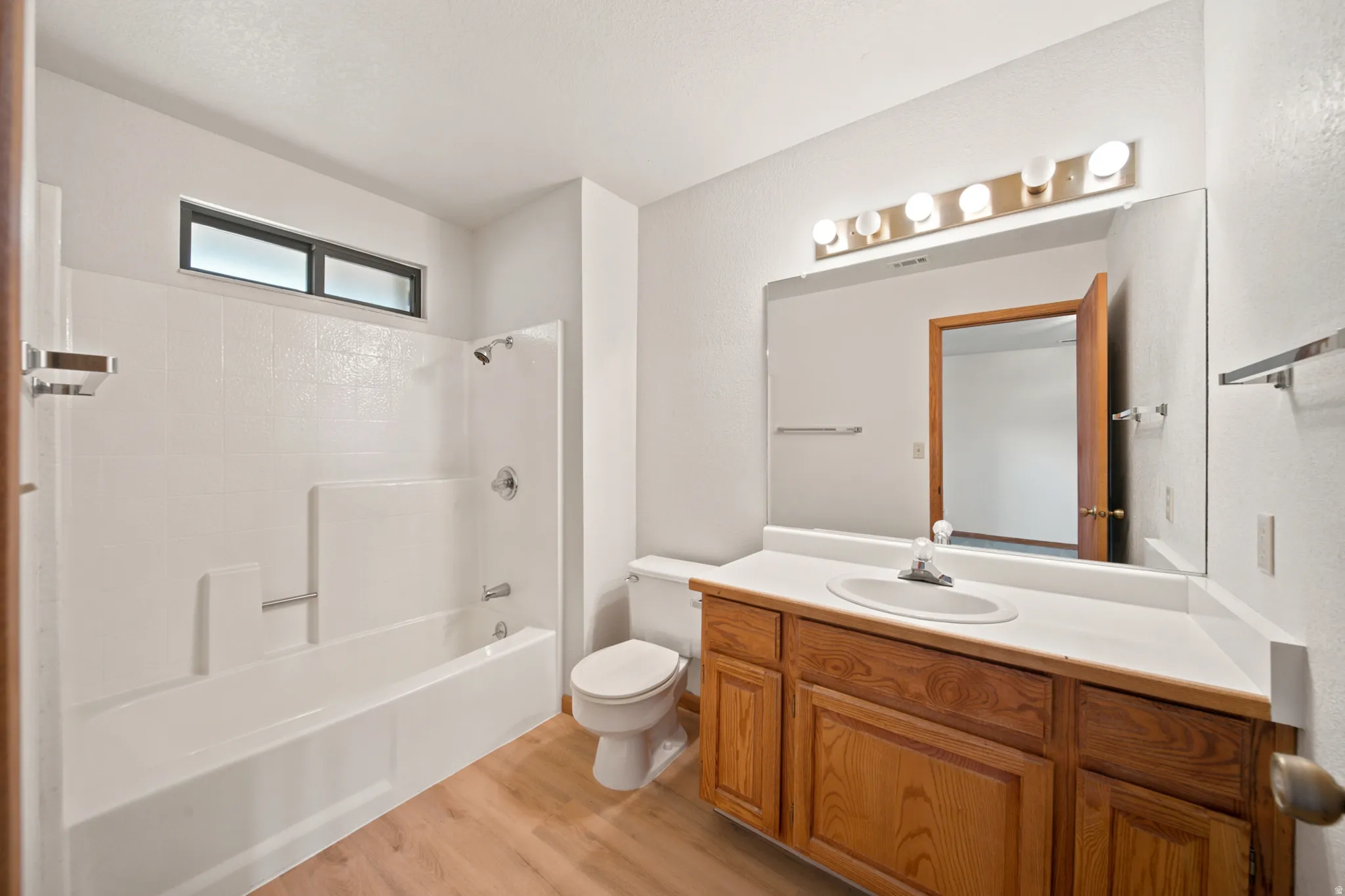 Full bathroom featuring a single vanity with wood-finish cabinetry, a large mirror, and a combined tub and shower with white surround