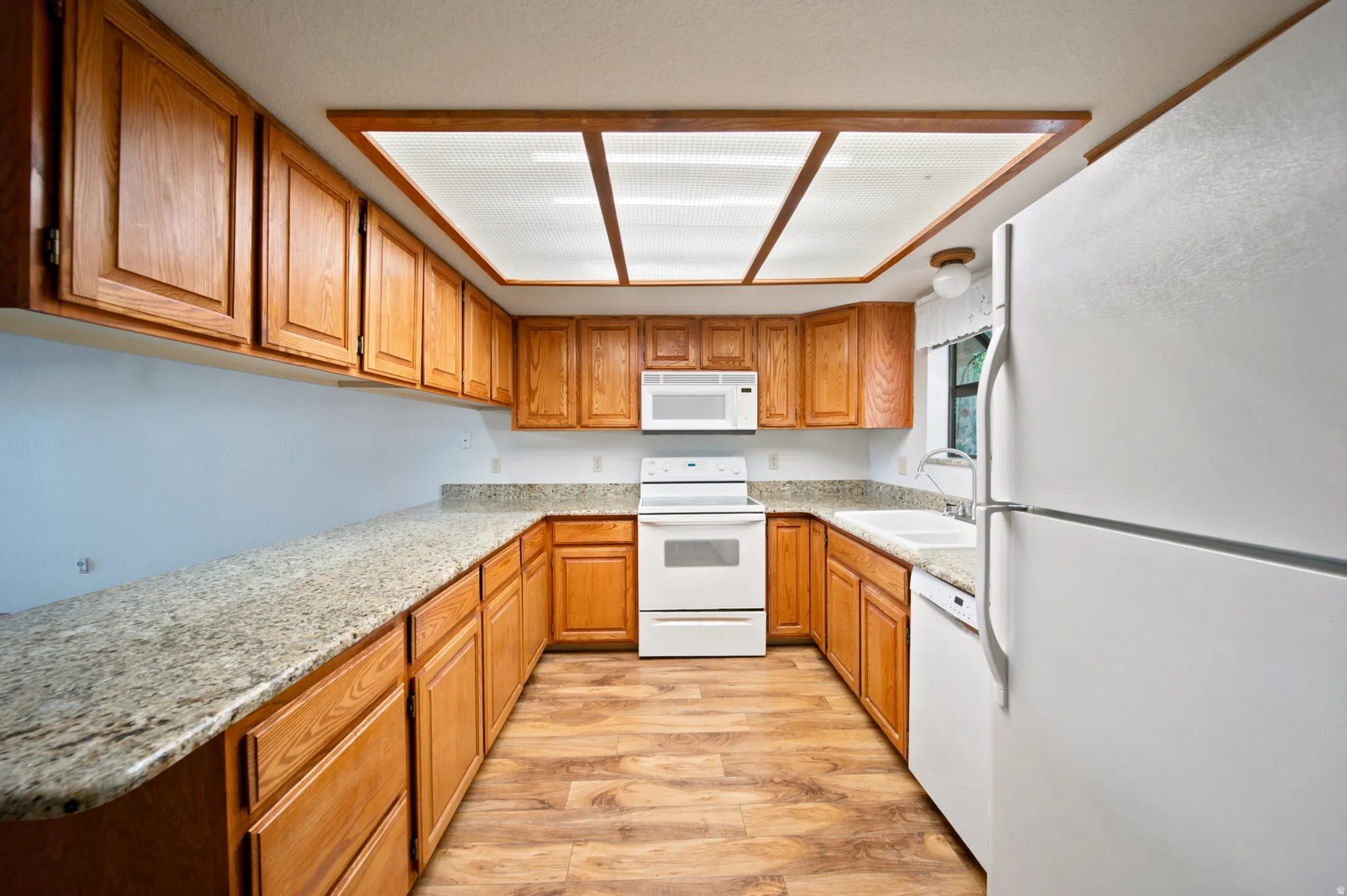 U-shaped kitchen featuring light wood cabinetry, stone-finish countertops, and wood-finish flooring