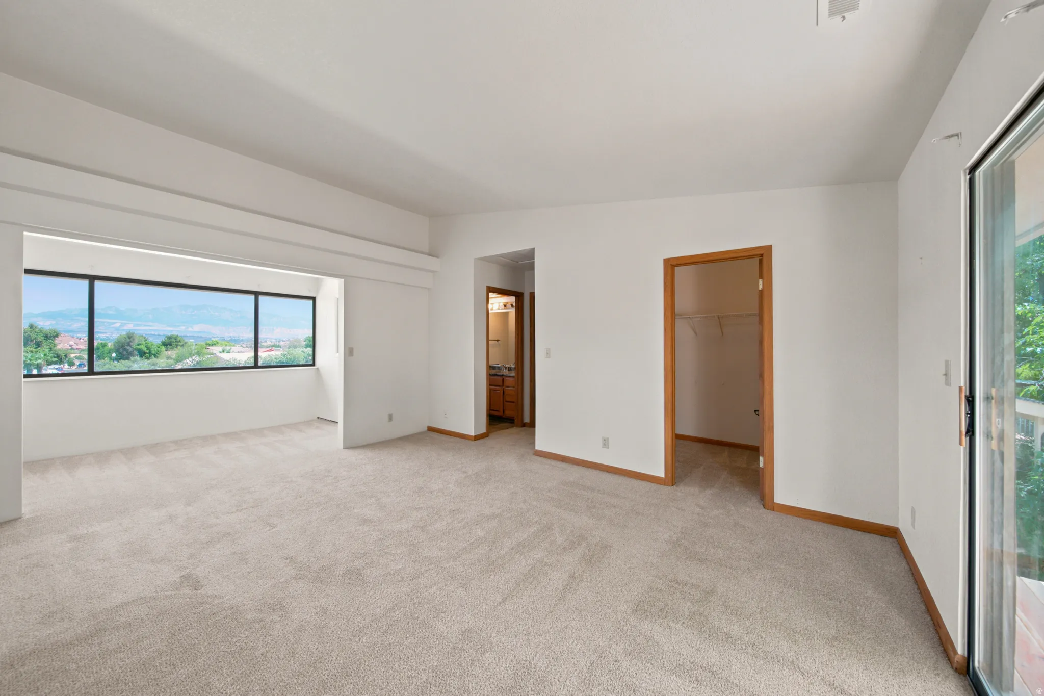 Spacious room featuring neutral carpeting, white walls, wood trim, and a large window offering expansive scenery